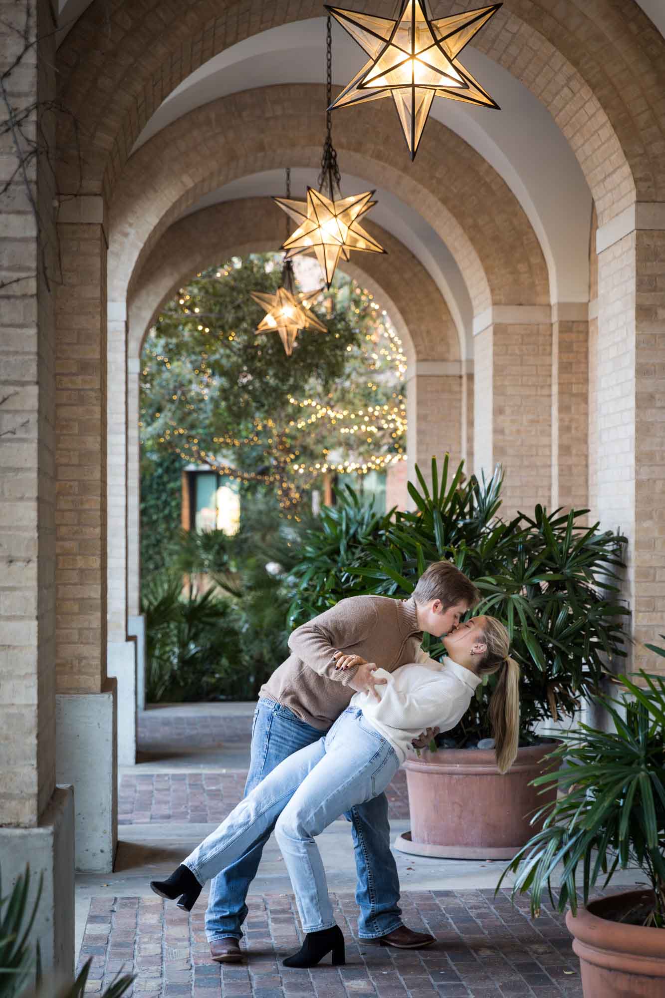 Couple wearing sweaters and dancing under brick arch with star lanterns at the Pearl during an engagement photo shoot