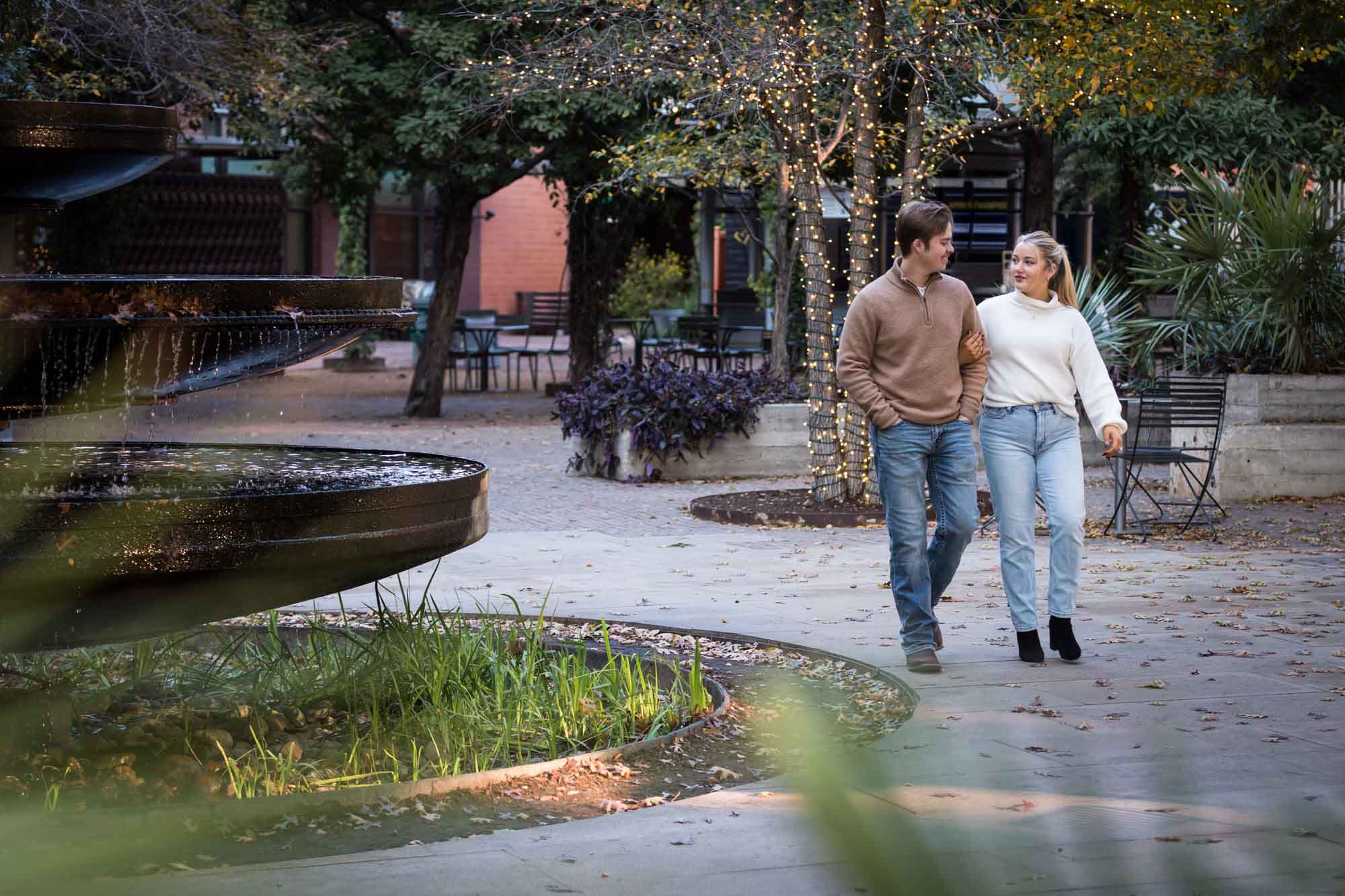 Couple wearing jeans and sweaters walking around a fountain at the historic Pearl in San Antonio