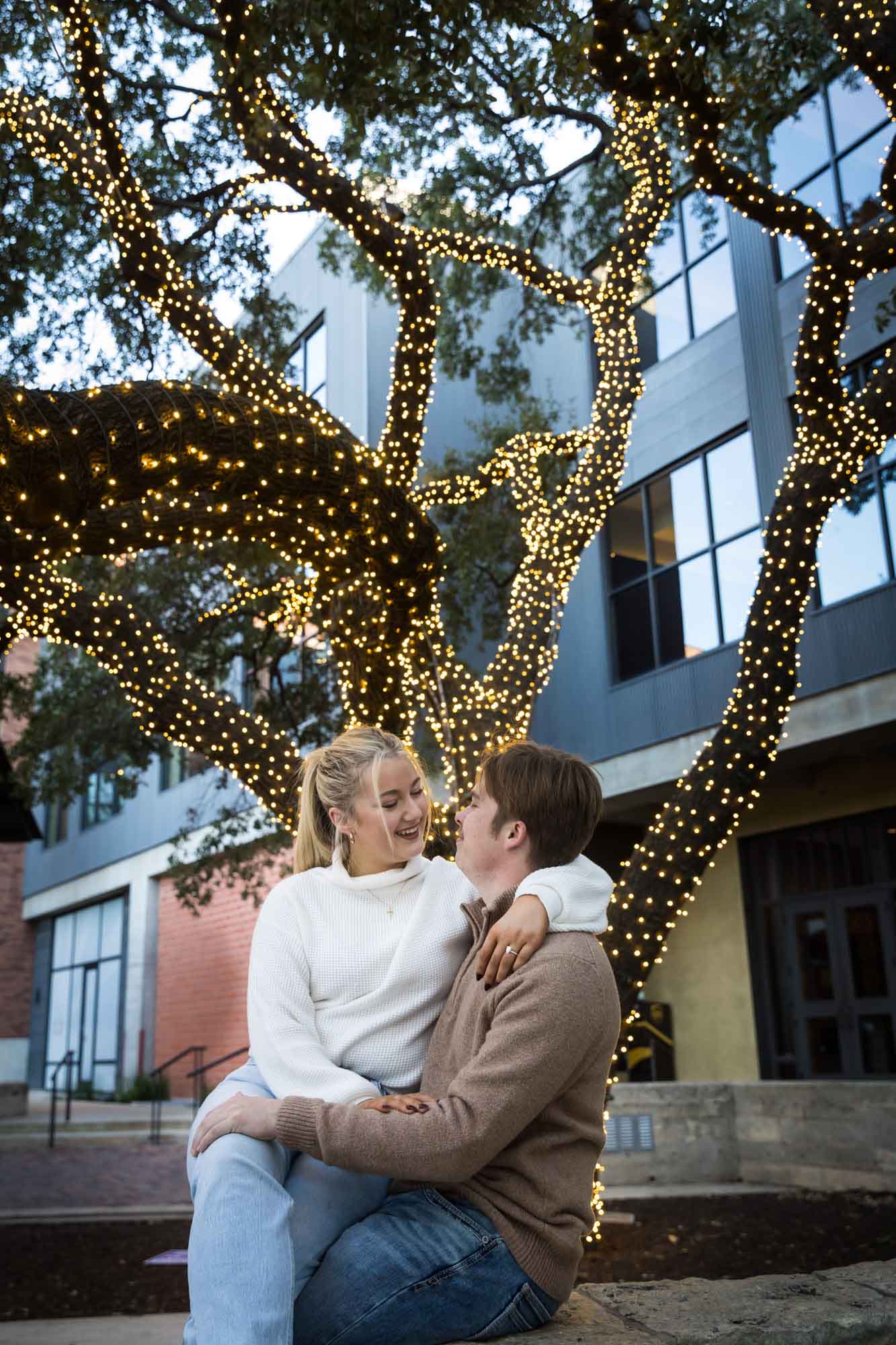 Couple hugging with tree wrapped in string lights in the background for an article on the importance of timing for a surprise proposal