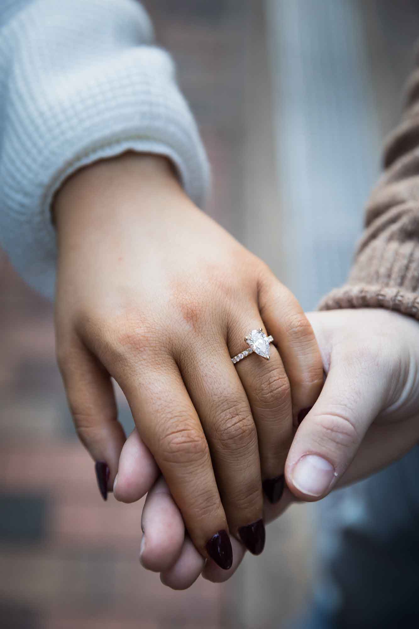 Close up of couple holding hands and showing woman wearing engagement ring