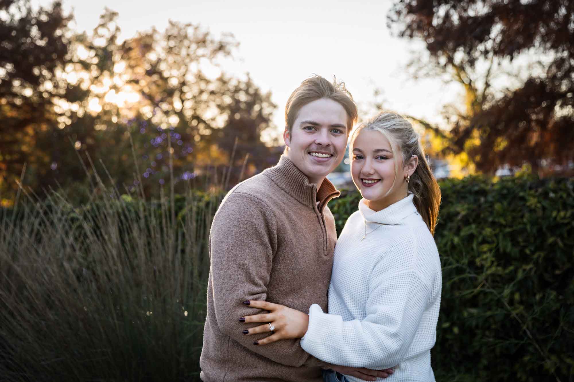 Couple hugging at sunset in front of bushes at the historic Pearl for an article on the importance of timing for a surprise proposal