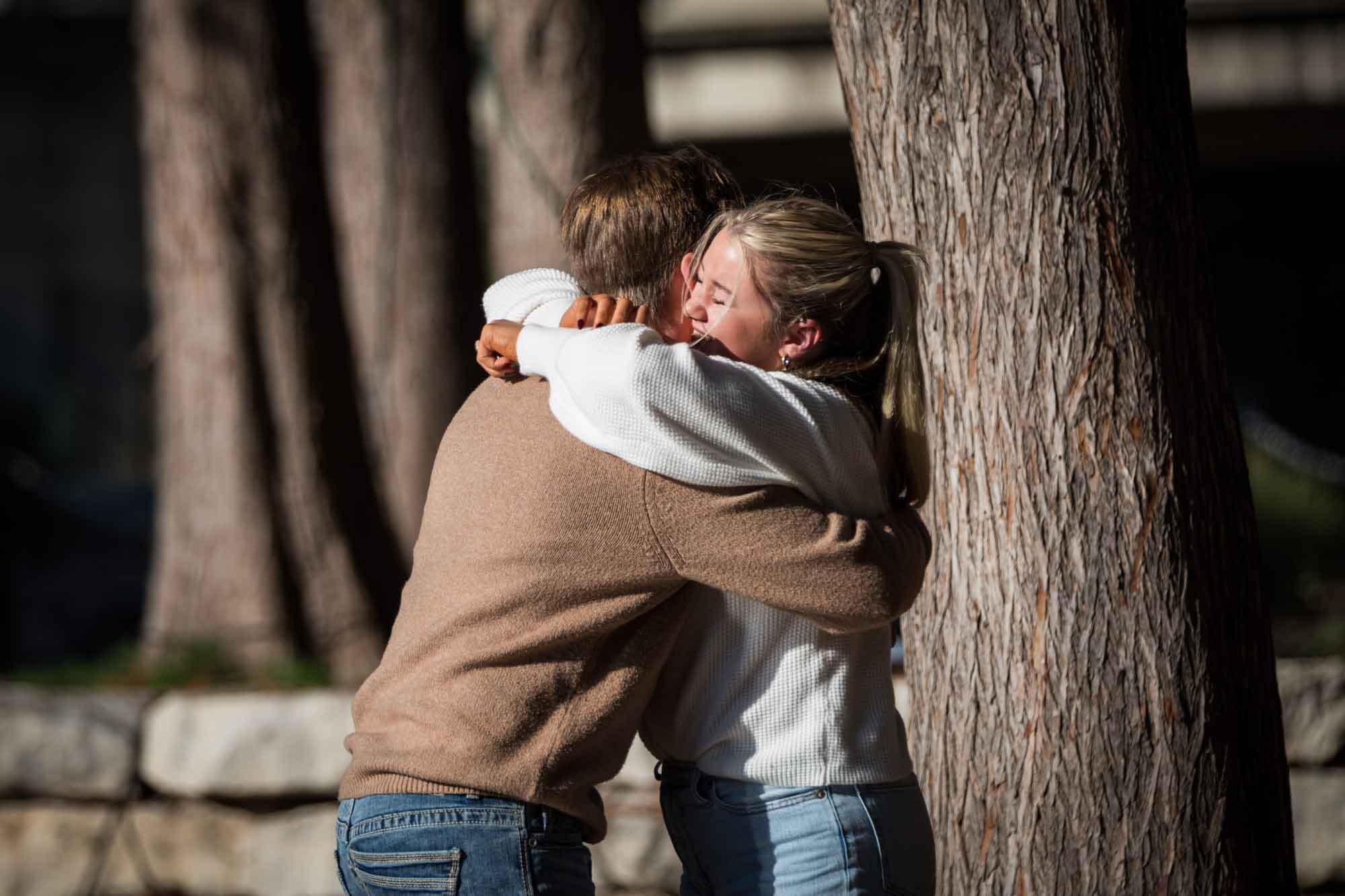 Couple hugging in front of trees for an article on the importance of timing for a surprise proposal