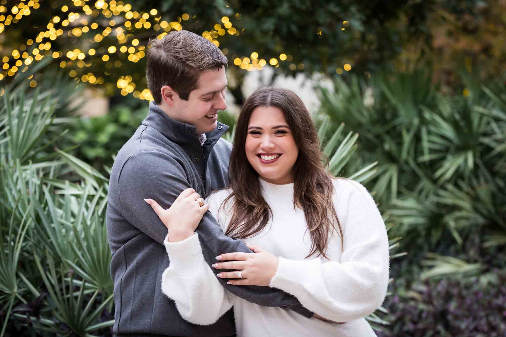 Couple hugging in front of green palm fronds during a surprise proposal at the Pearl