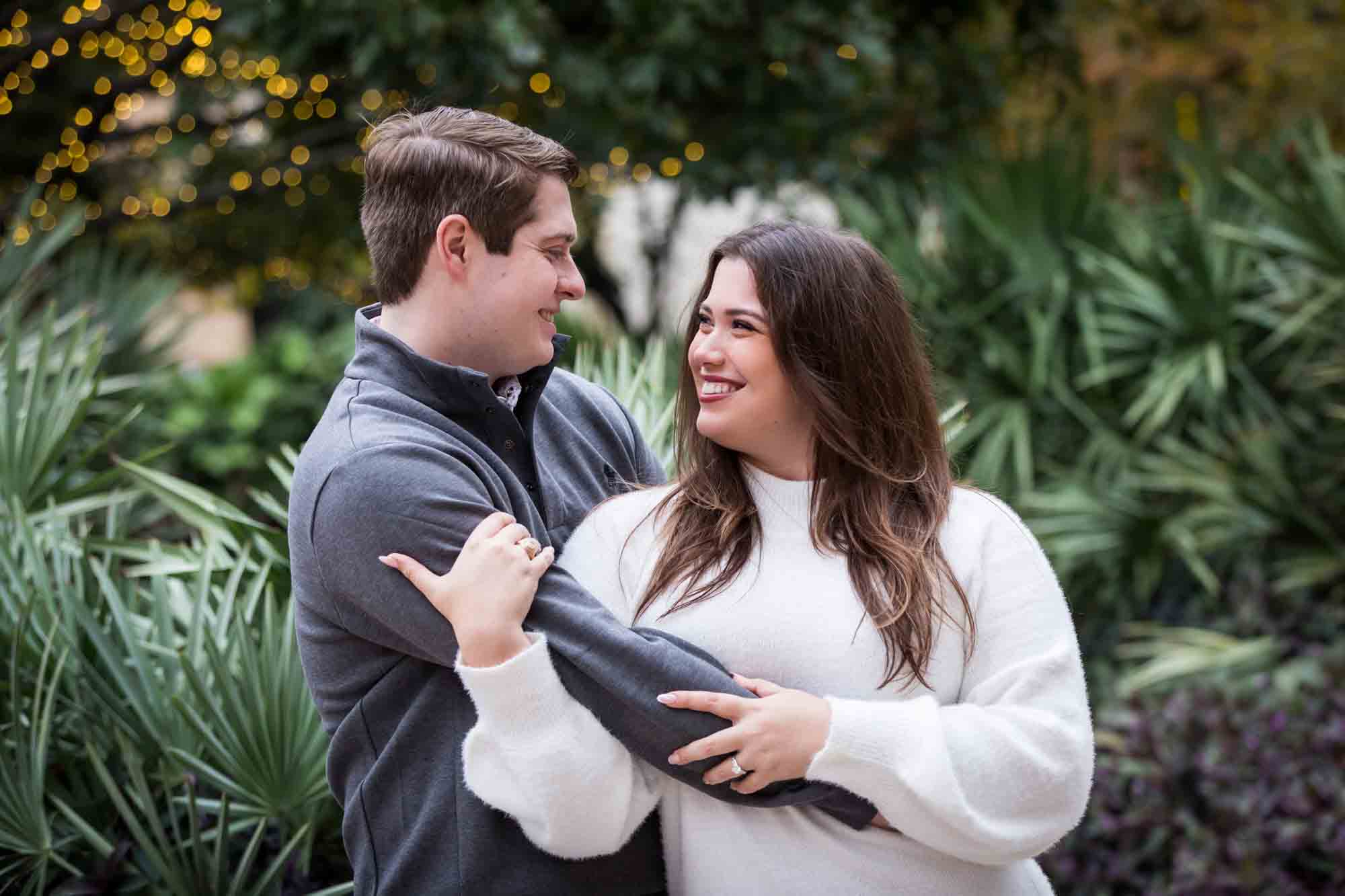 Couple hugging in front of green palm fronds during a surprise proposal at the Pearl