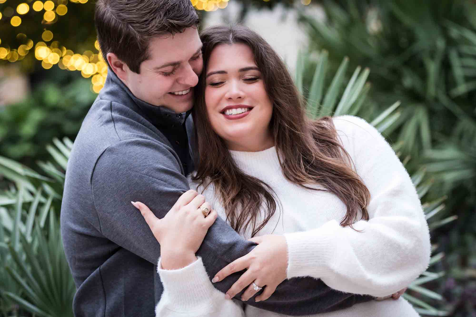 Couple hugging in front of green palm fronds during a surprise proposal at the Pearl