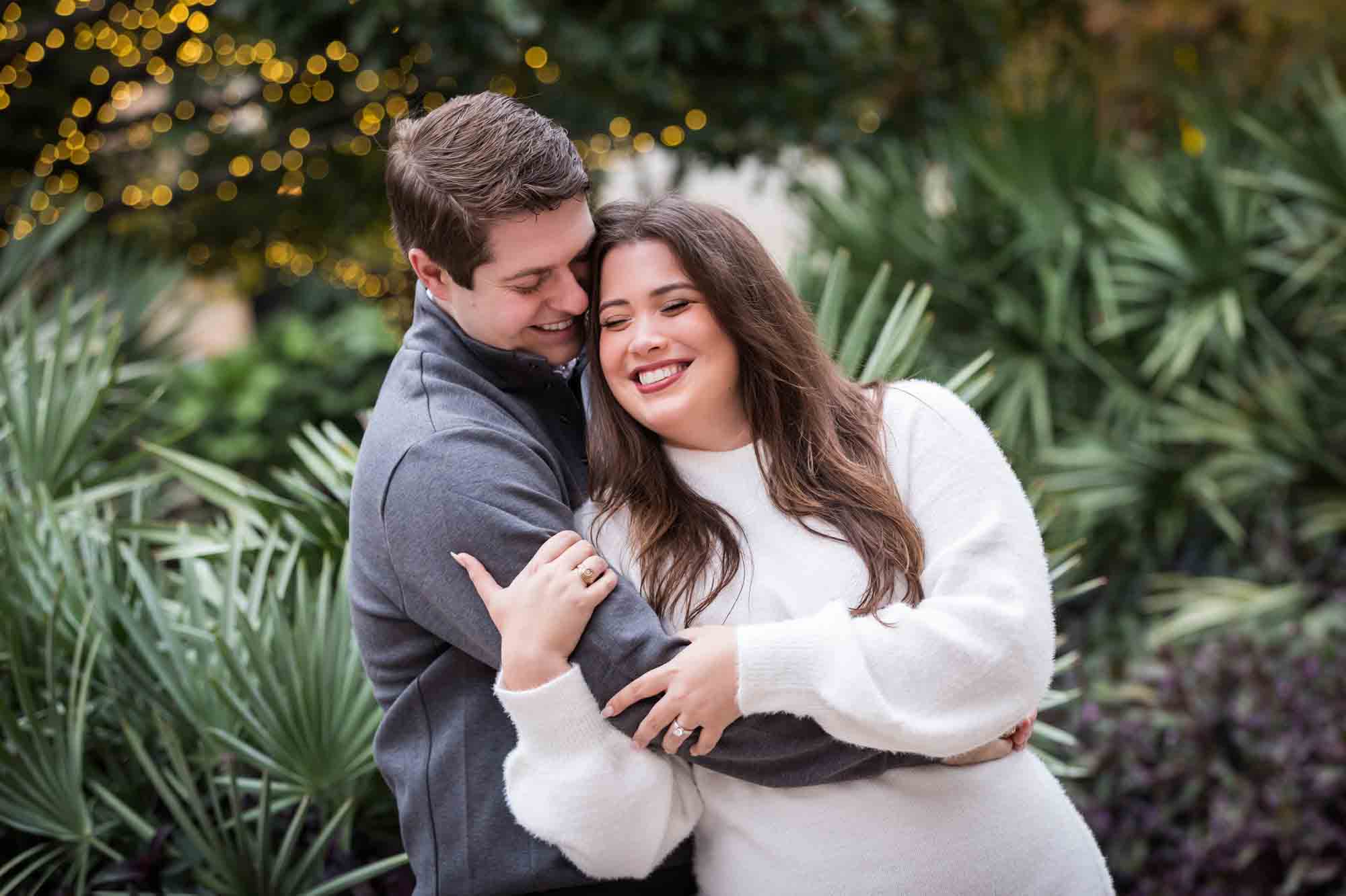 Couple hugging in front of green palm fronds during a surprise proposal at the Pearl