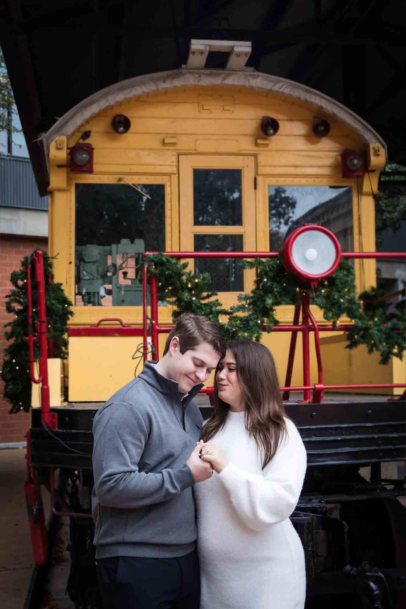 Couple looking at engagement ring in front of yellow train trolley during a surprise proposal at the Pearl