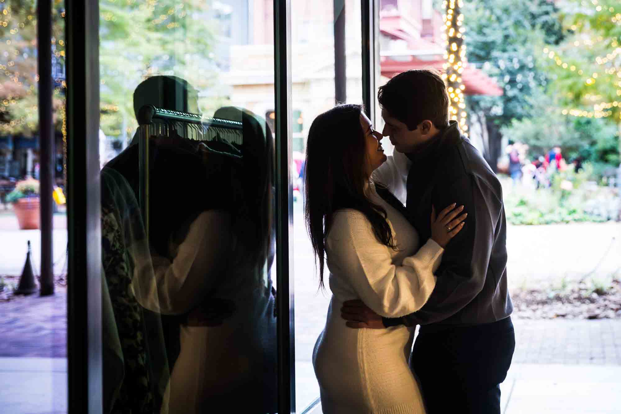 Backlit reflection of couple against glass window during a surprise proposal at the Pearl