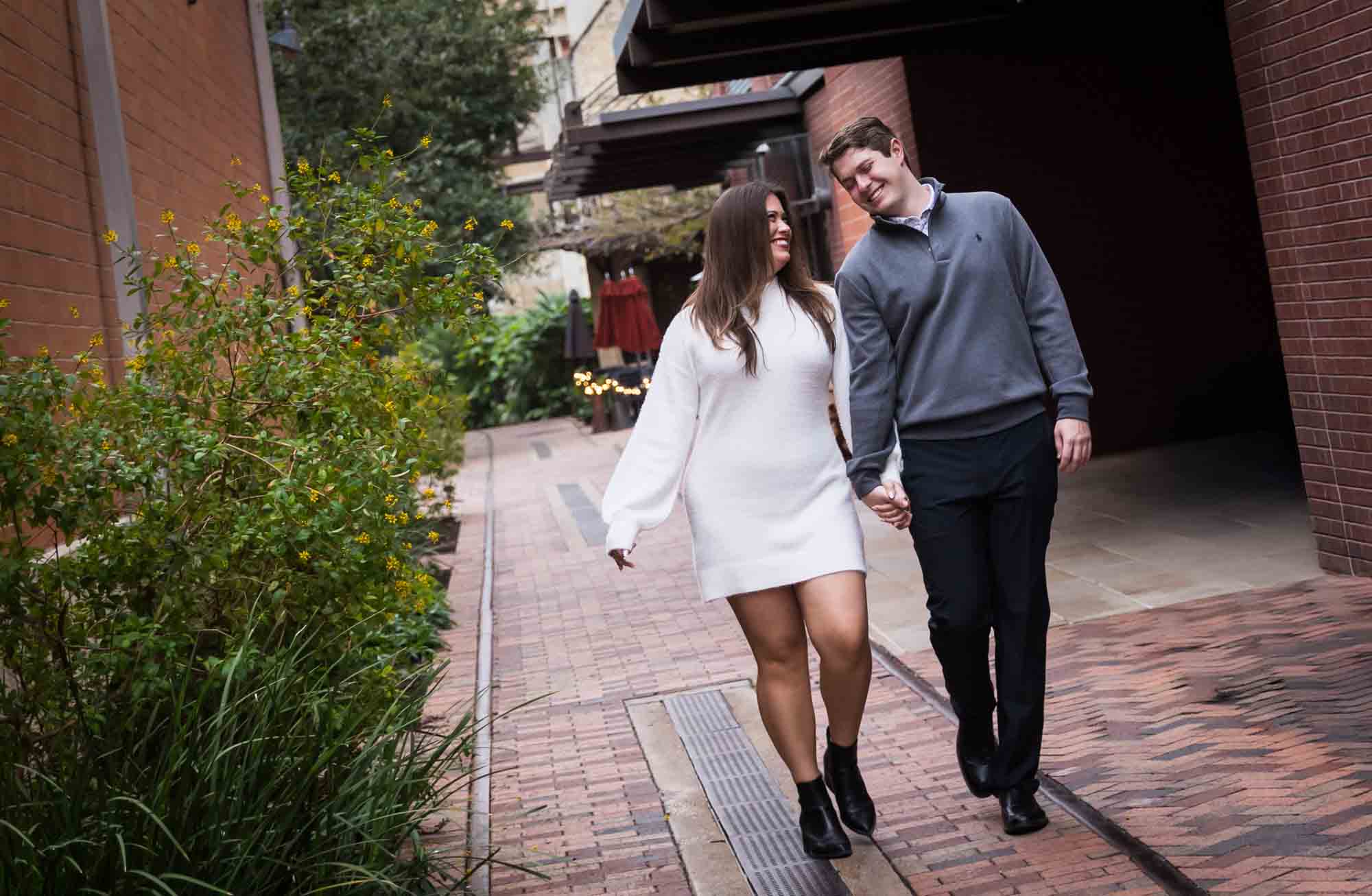 Couple walking down alleyway with Historic Pearl building in background during an engagement photo shoot at the Pearl