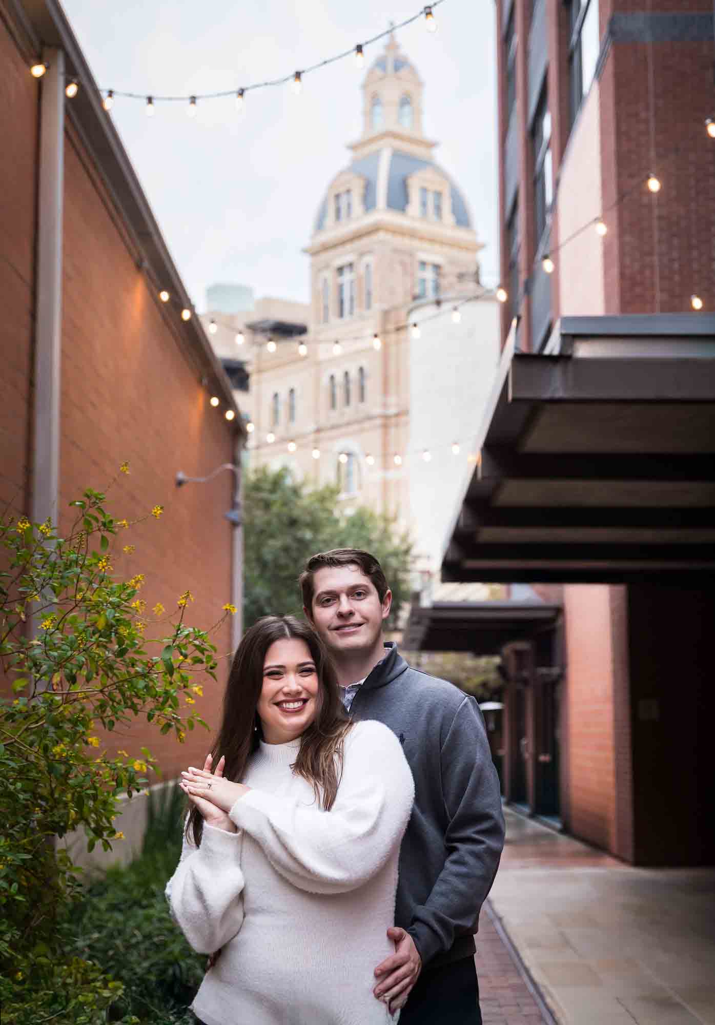 Couple hugging in alleyway with Historic Pearl building in background during an engagement photo shoot at the Pearl