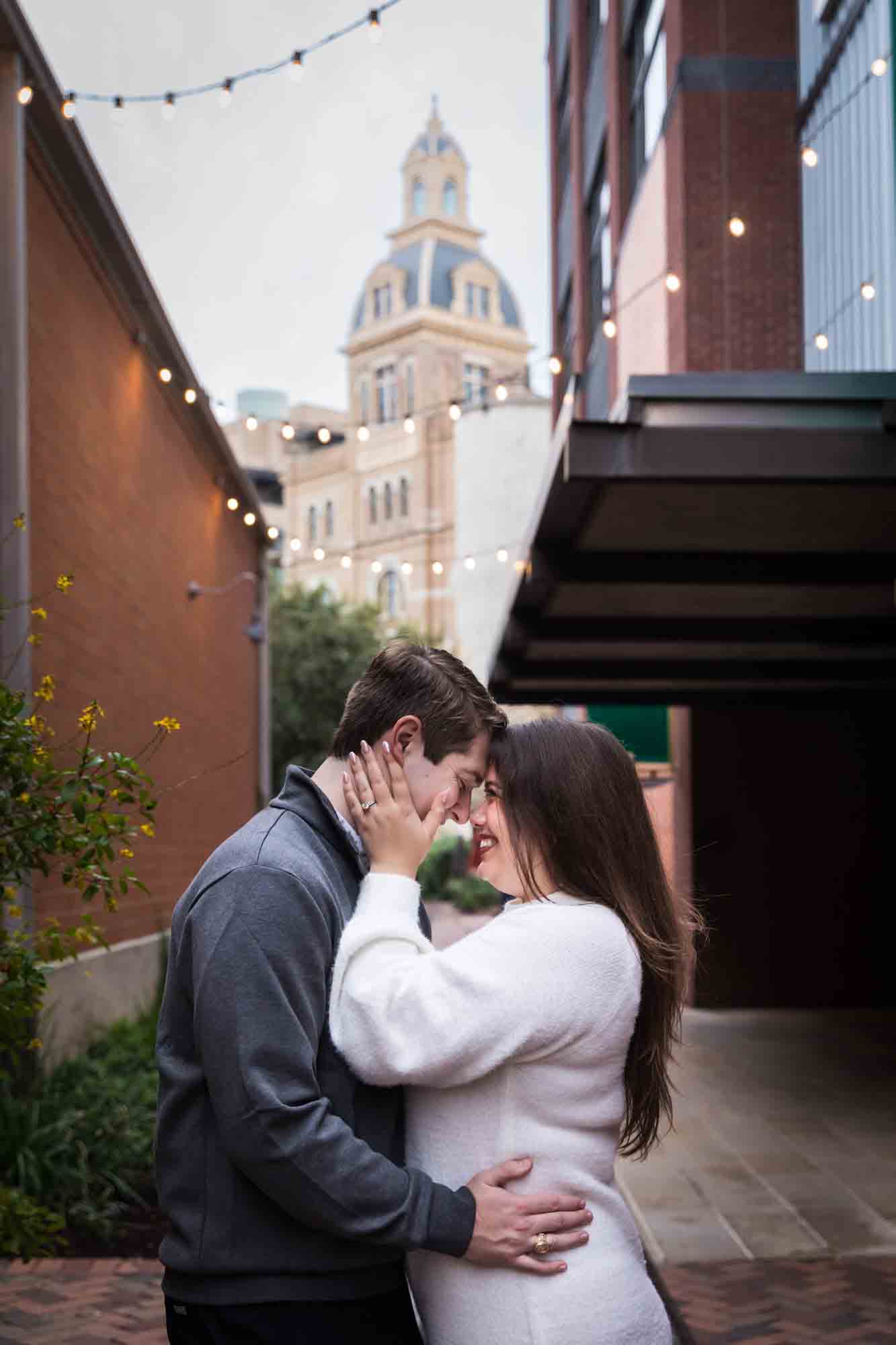 Couple hugging in alleyway with Historic Pearl building in background during an engagement photo shoot at the Pearl