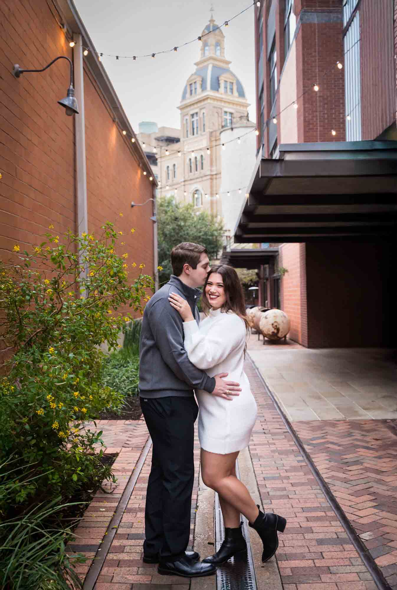 Couple hugging in alleyway with Historic Pearl building in background during an engagement photo shoot at the Pearl