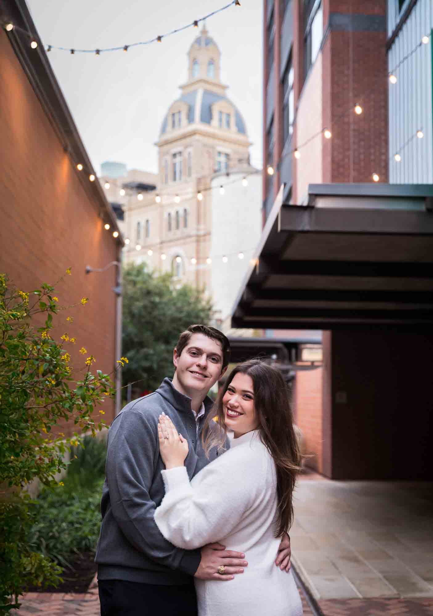 Couple hugging in alleyway with Historic Pearl building in background during an engagement photo shoot at the Pearl