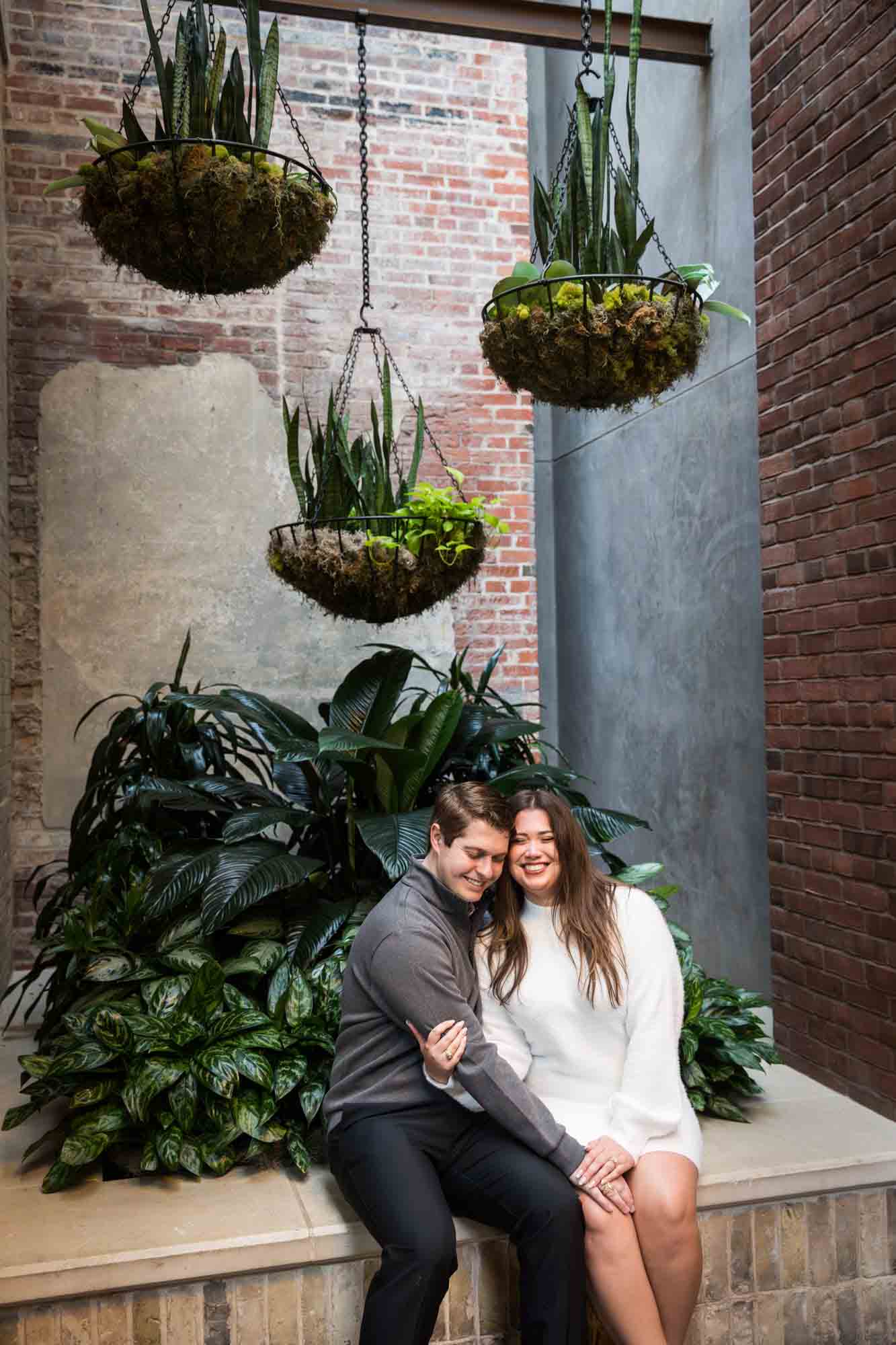 Couple seated by decorative plants during an engagement photo shoot at the Pearl