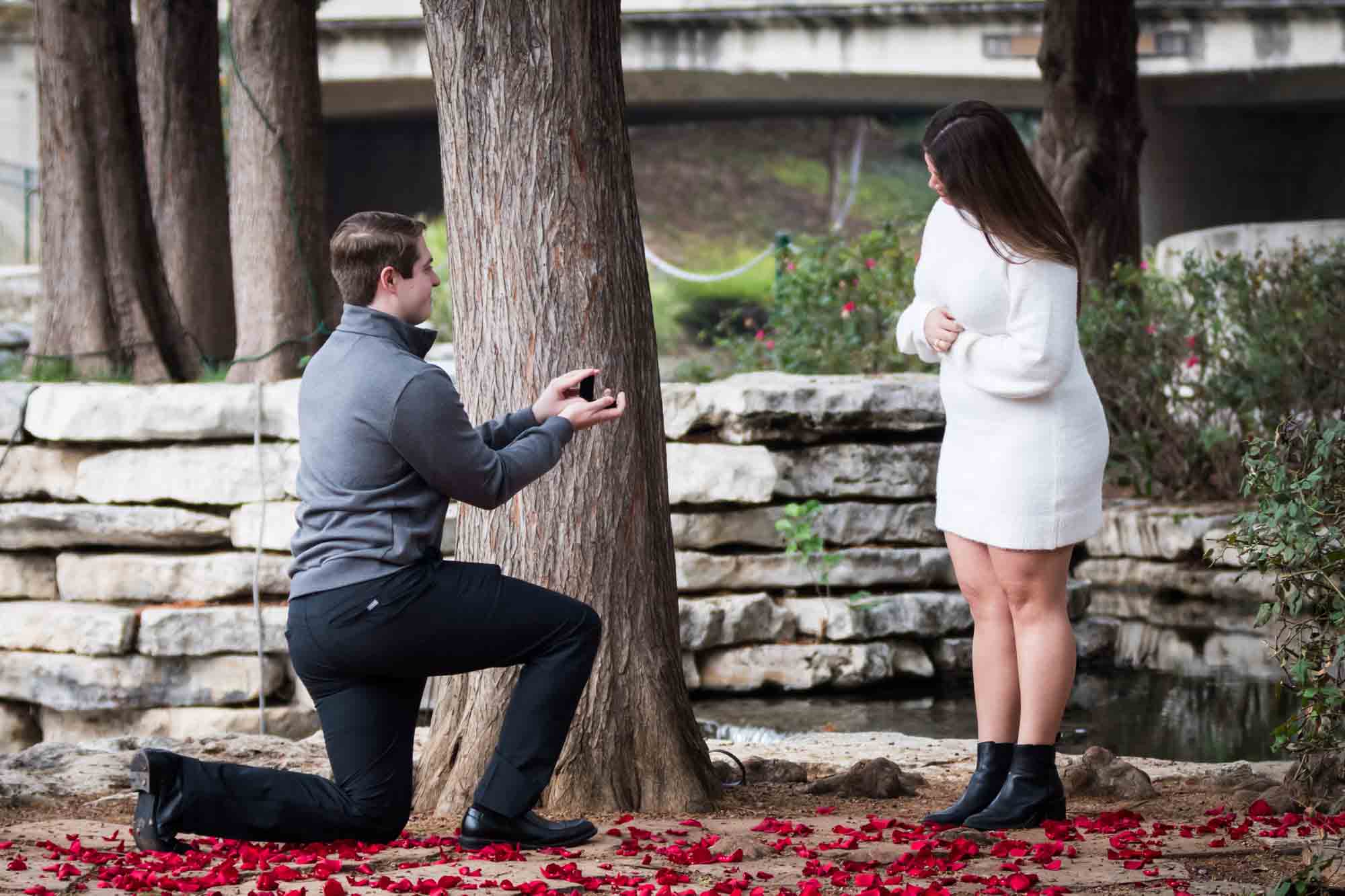 Man proposing on one knee during a surprise proposal at the Pearl