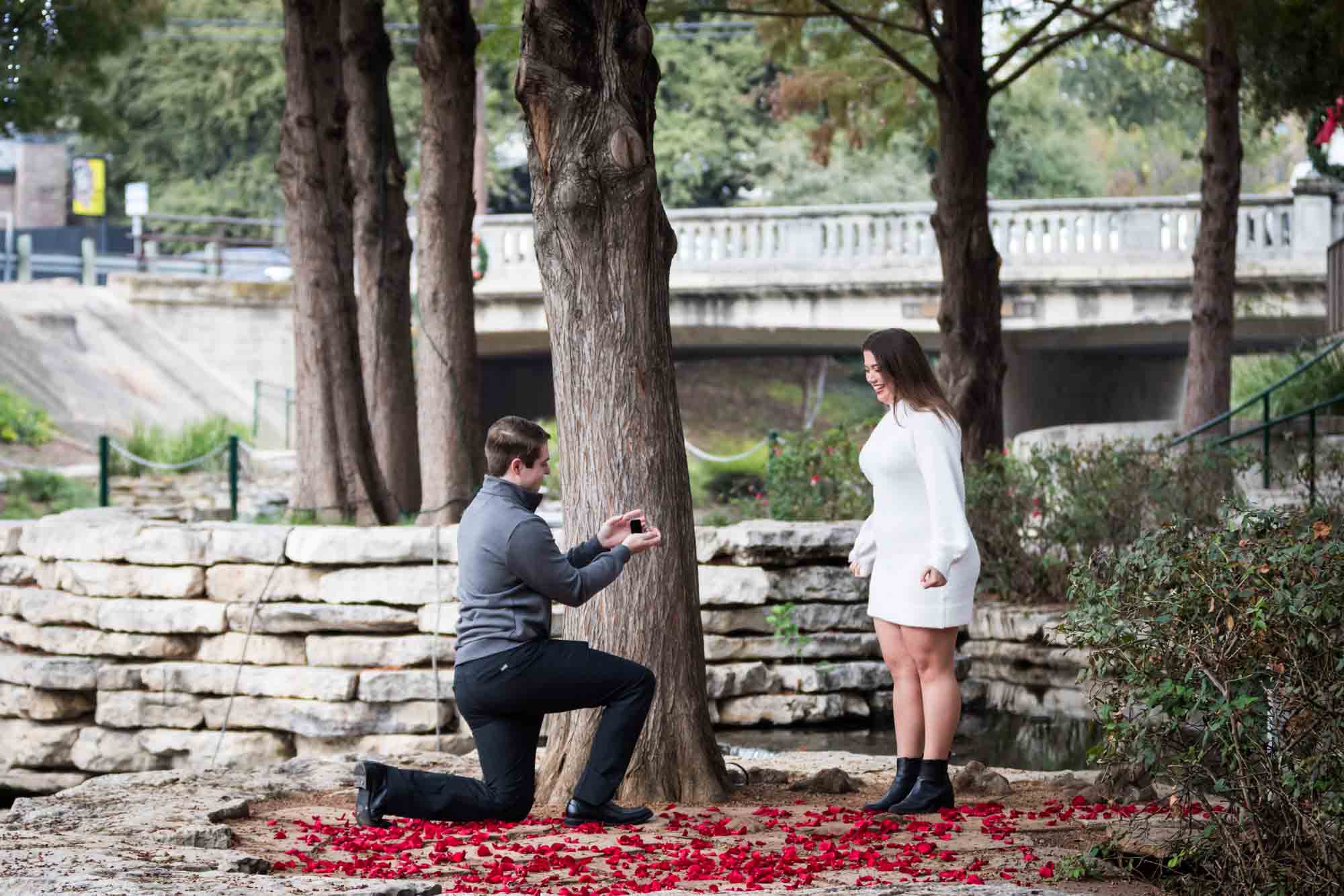 Man proposing on one knee during a surprise proposal at the Pearl