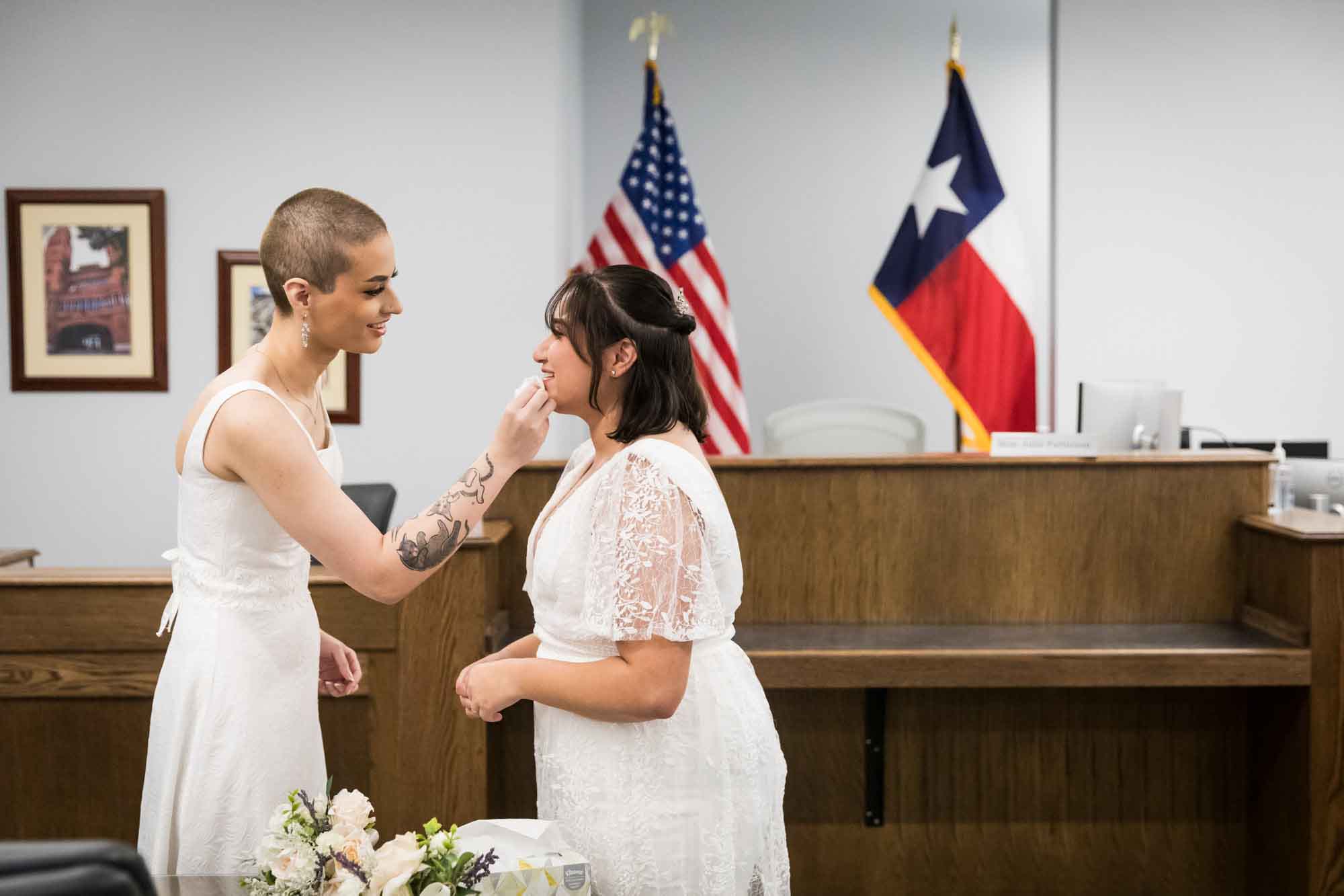 Bride wiping away tears of another bride during wedding ceremony at Bexar County Courthouse Precinct 3