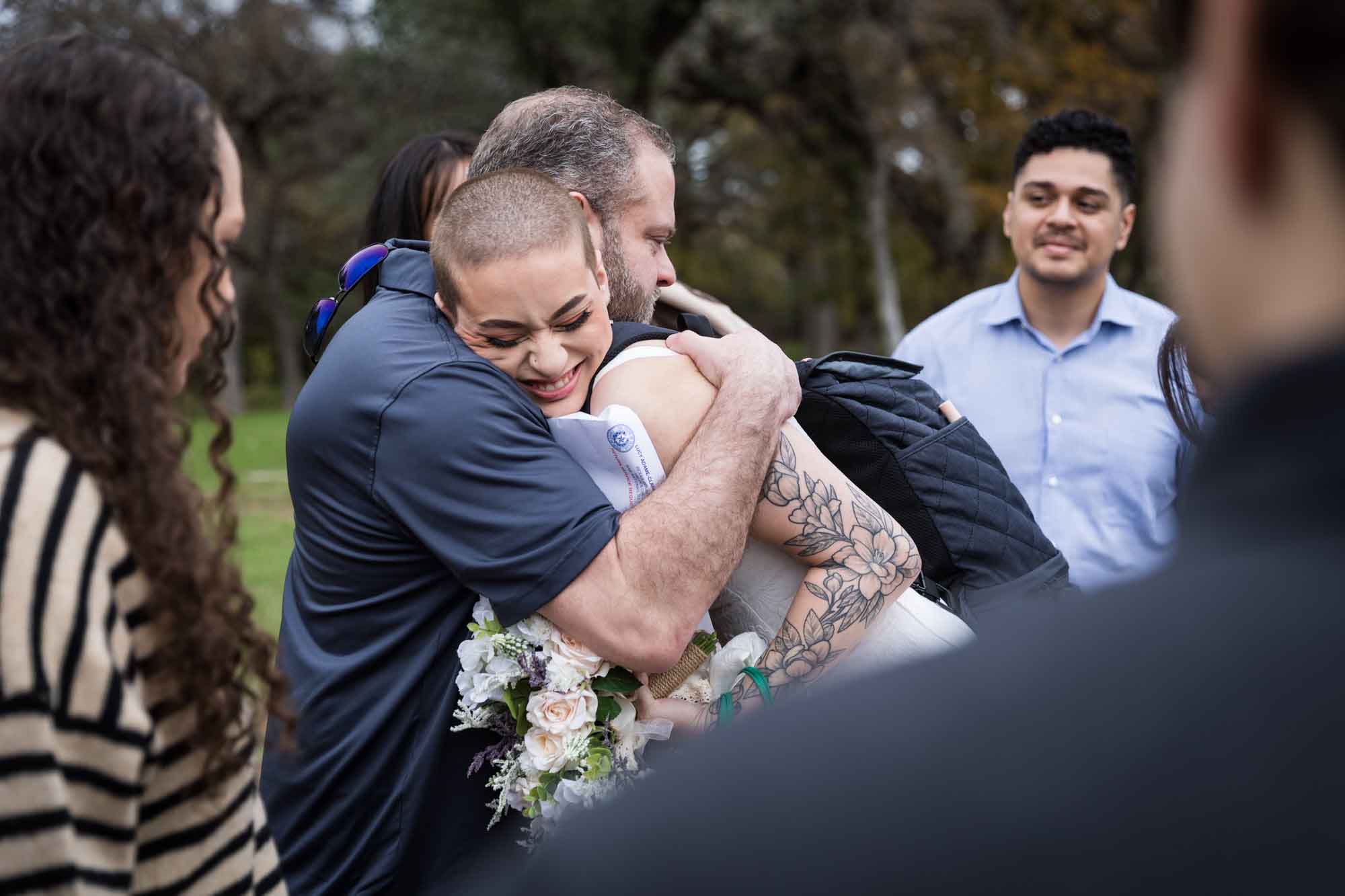 Father hugging bride with shaved head in parking lot