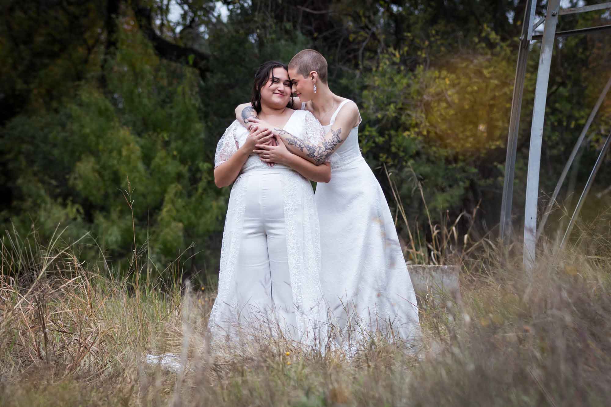 Walker Ranch Park wedding photos of two brides dressed in white hugging in grass meadow