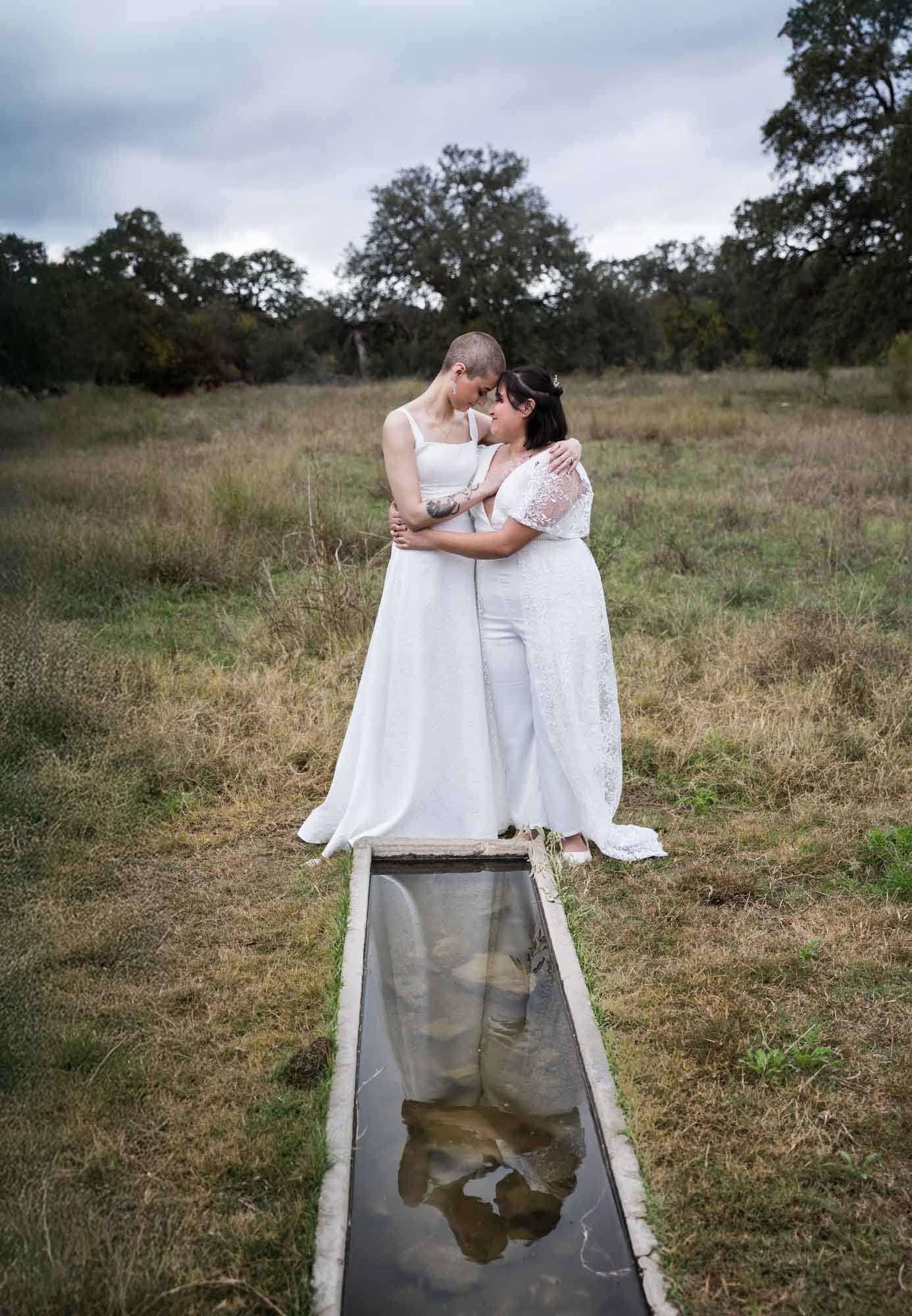 Walker Ranch Park wedding photos of two brides dressed in white hugging with reflection in water trough