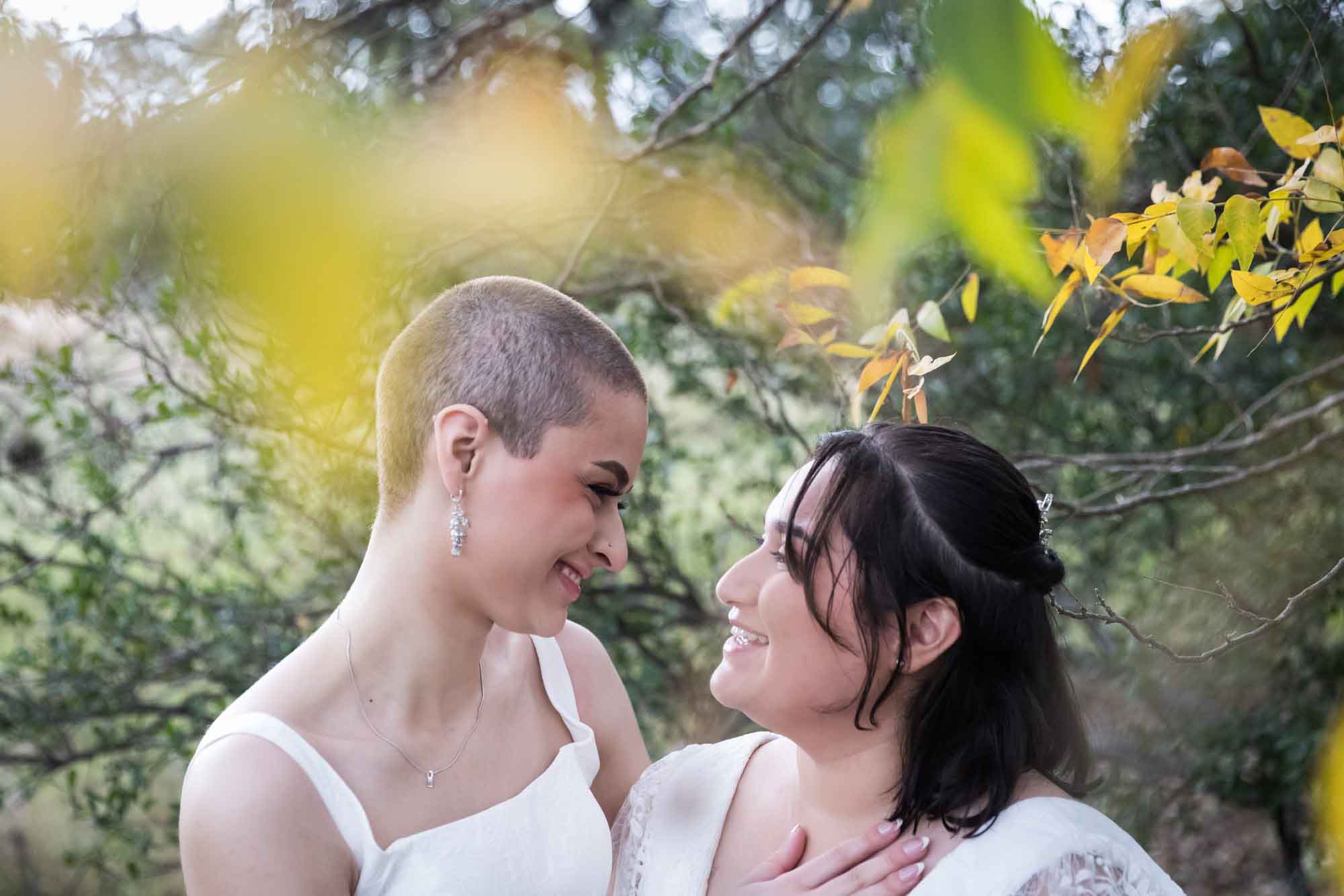 Walker Ranch Park wedding photos of two brides dressed in white hugging as viewed through yellow leaves