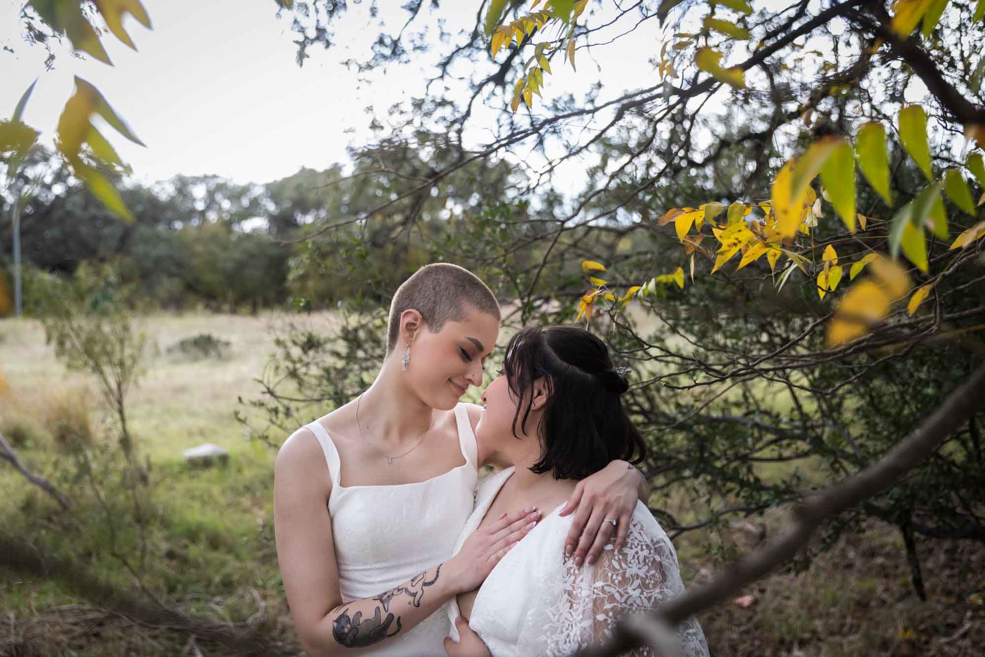 Walker Ranch Park wedding photos of two brides dressed in white hugging under tree branch