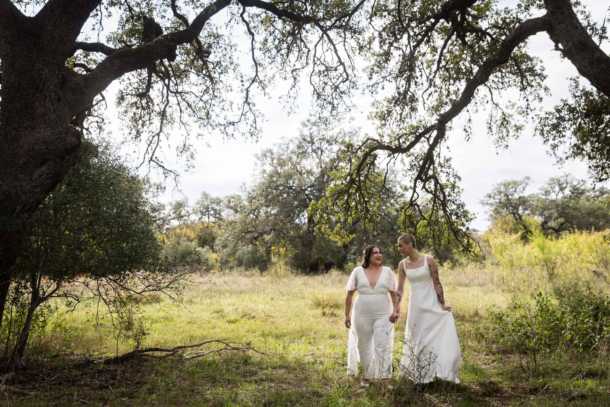 Walker Ranch Park wedding photos of two brides dressed in white walking across meadow under tree branch