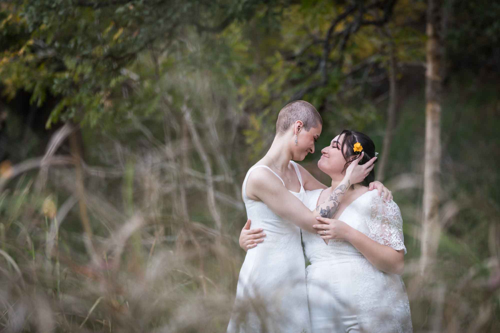 Walker Ranch Park wedding photos of two brides dressed in white hugging in front of forest and grass