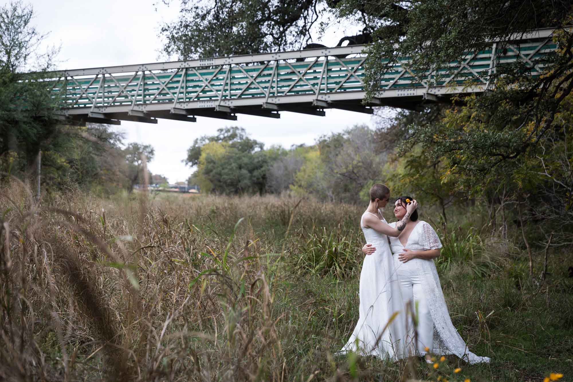 Walker Ranch Park wedding photos of two brides dressed in white hugging in front of grass and bridge