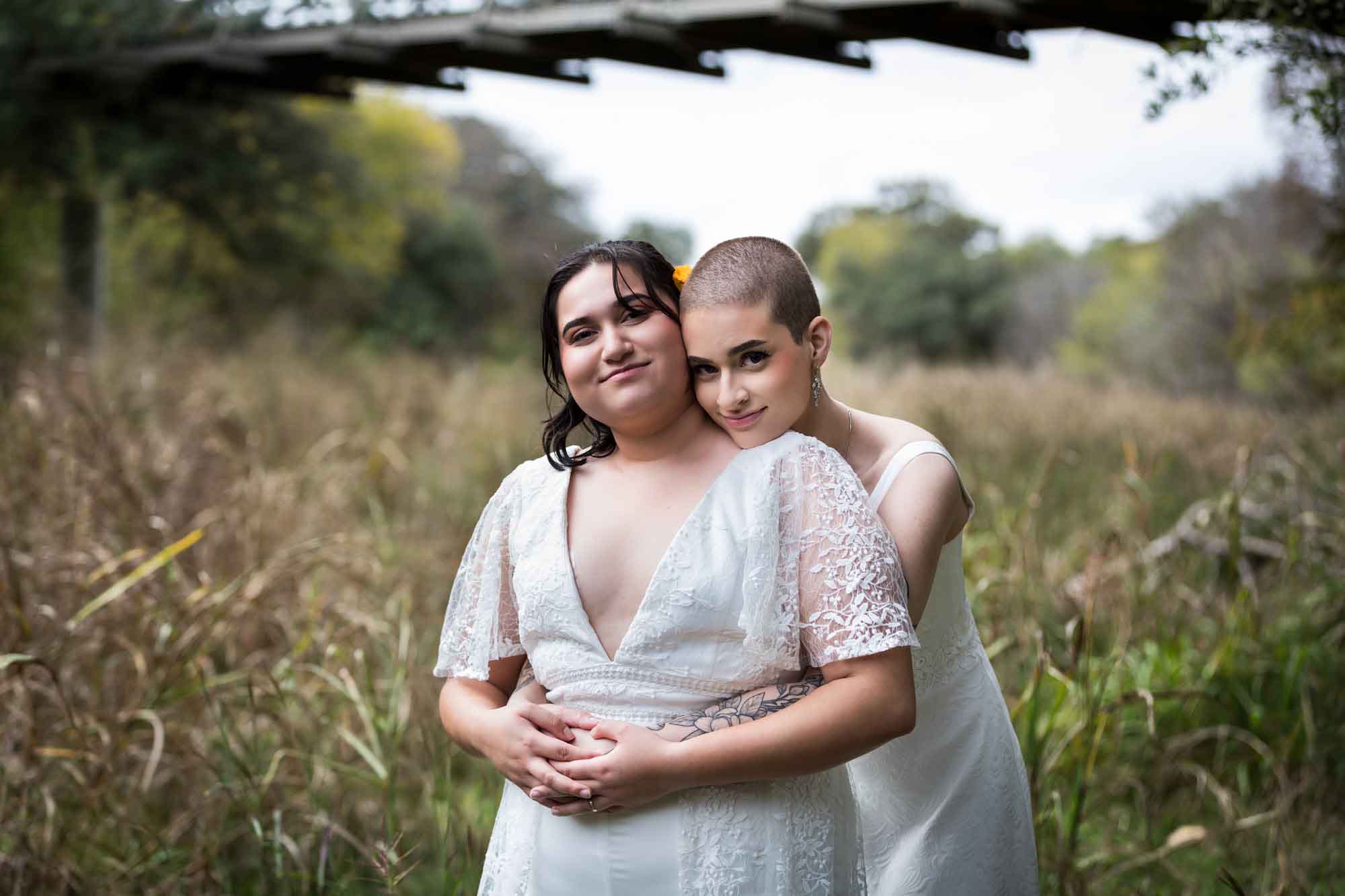 Walker Ranch Park wedding photos of two brides dressed in white hugging in grass