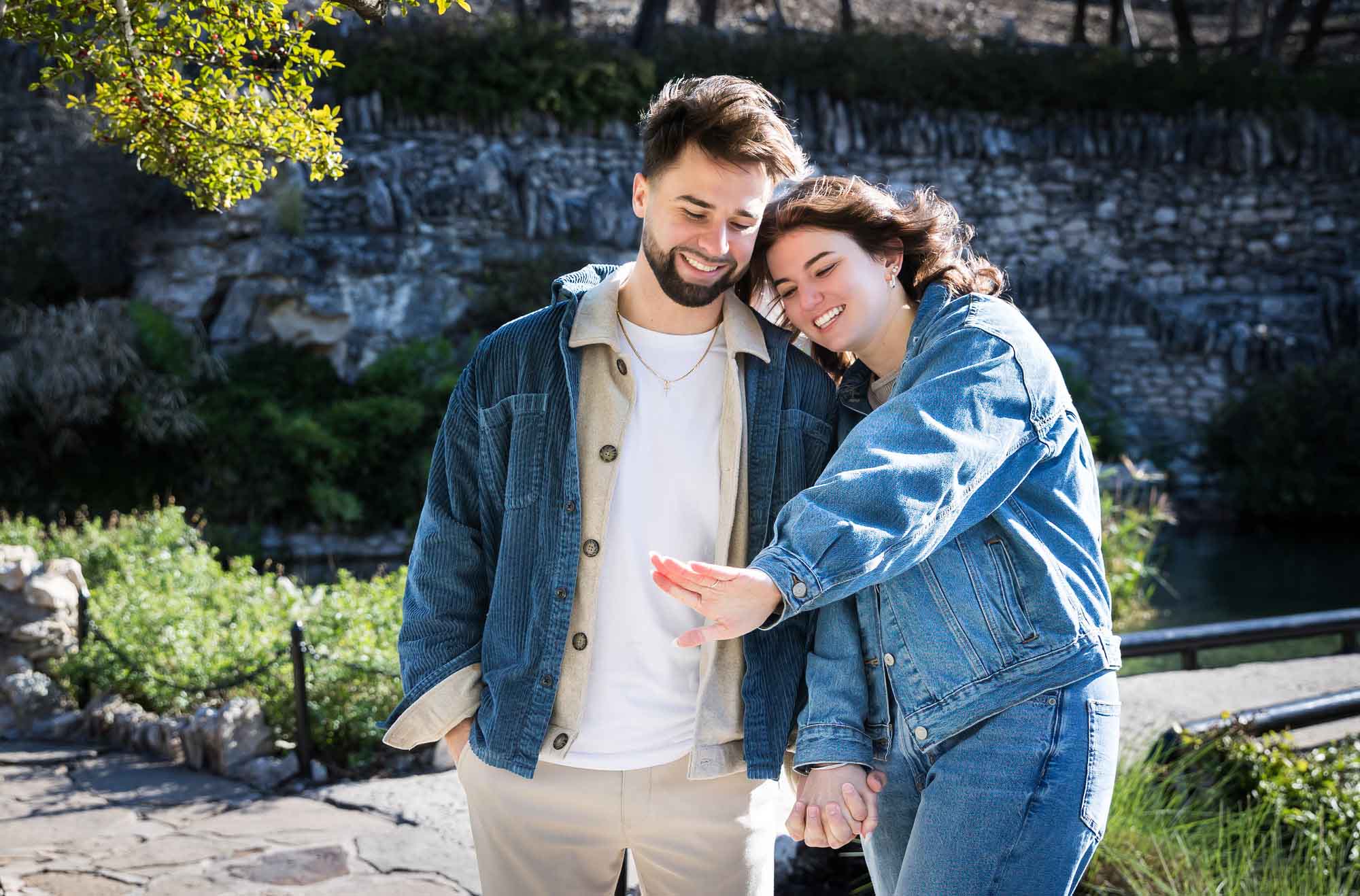 Woman showing hand wearing engagement ring to man in garden during a Japanese Tea Garden surprise proposal