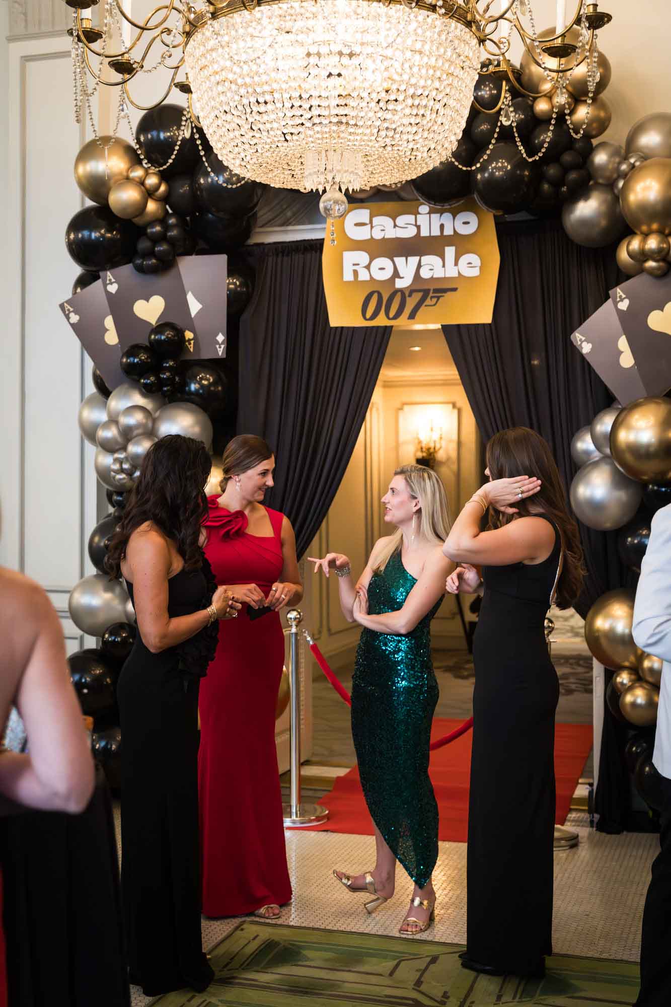 Four women speaking in front of balloon sculpture under glass chandelier for an article on a St. Anthony Hotel corporate event