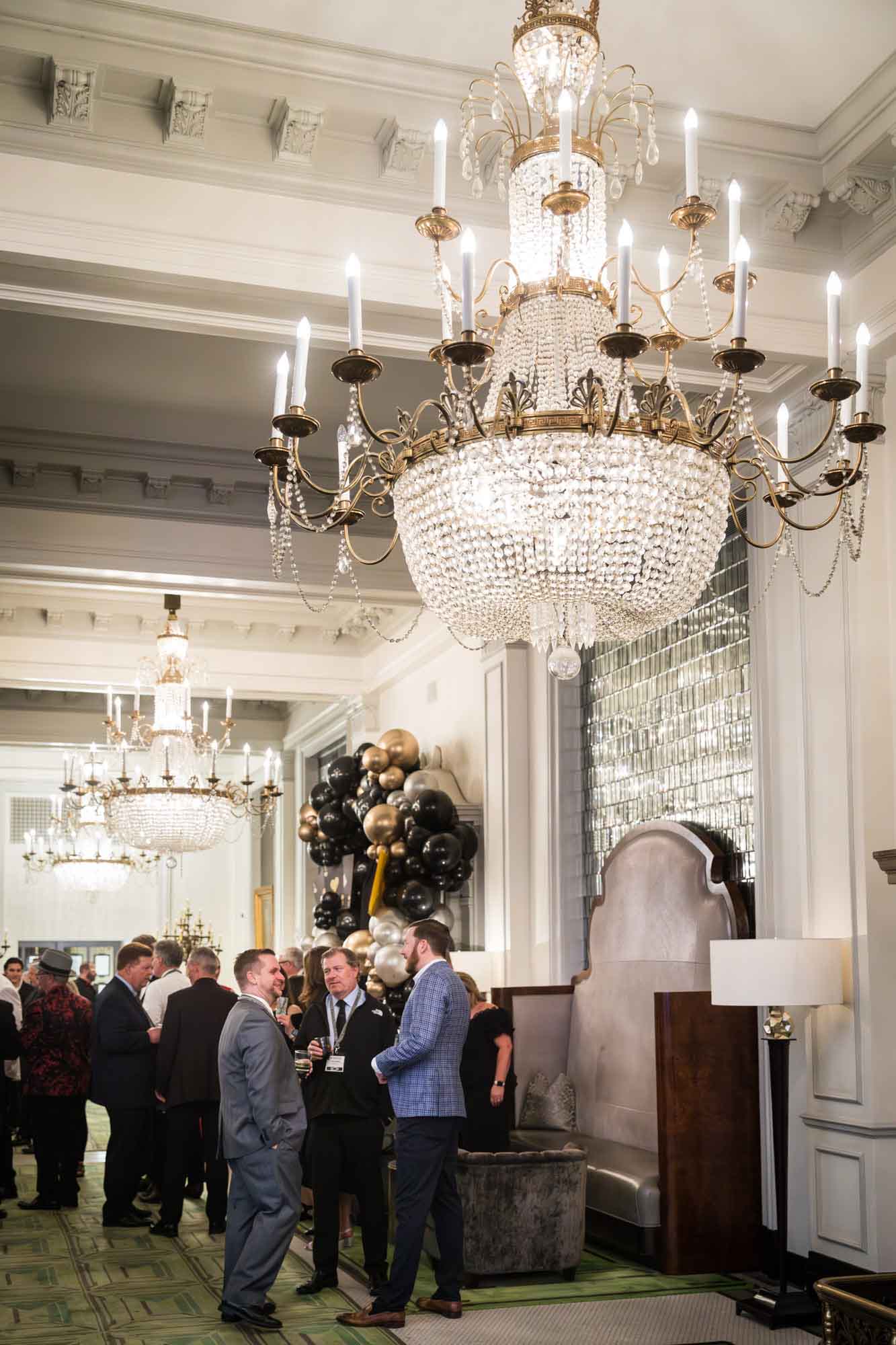 Guests enjoying cocktail hour in the Peacock Alley under giant glass chandeliers for an article on a St. Anthony Hotel corporate event