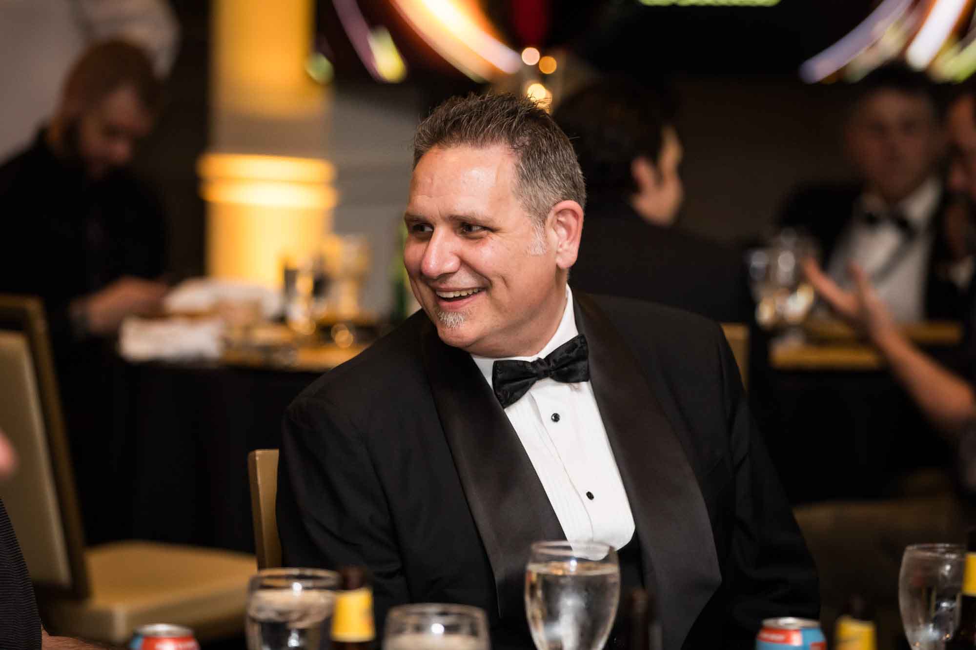 Man wearing black tuxedo and bow tie smiling while seated at table for an article on a St. Anthony Hotel corporate event