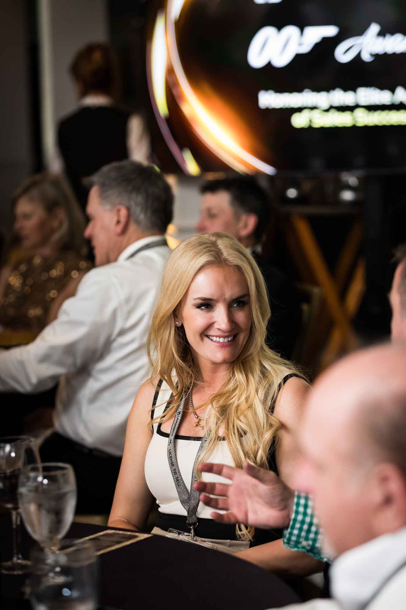 Blonde-haired woman smiling at other guests while seated at table for an article on a St. Anthony Hotel corporate event