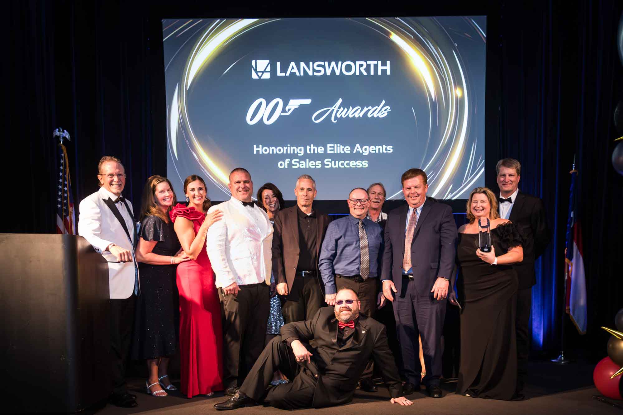 Line of award winners behind man lying on floor with screen in background for an article on a St. Anthony Hotel corporate event
