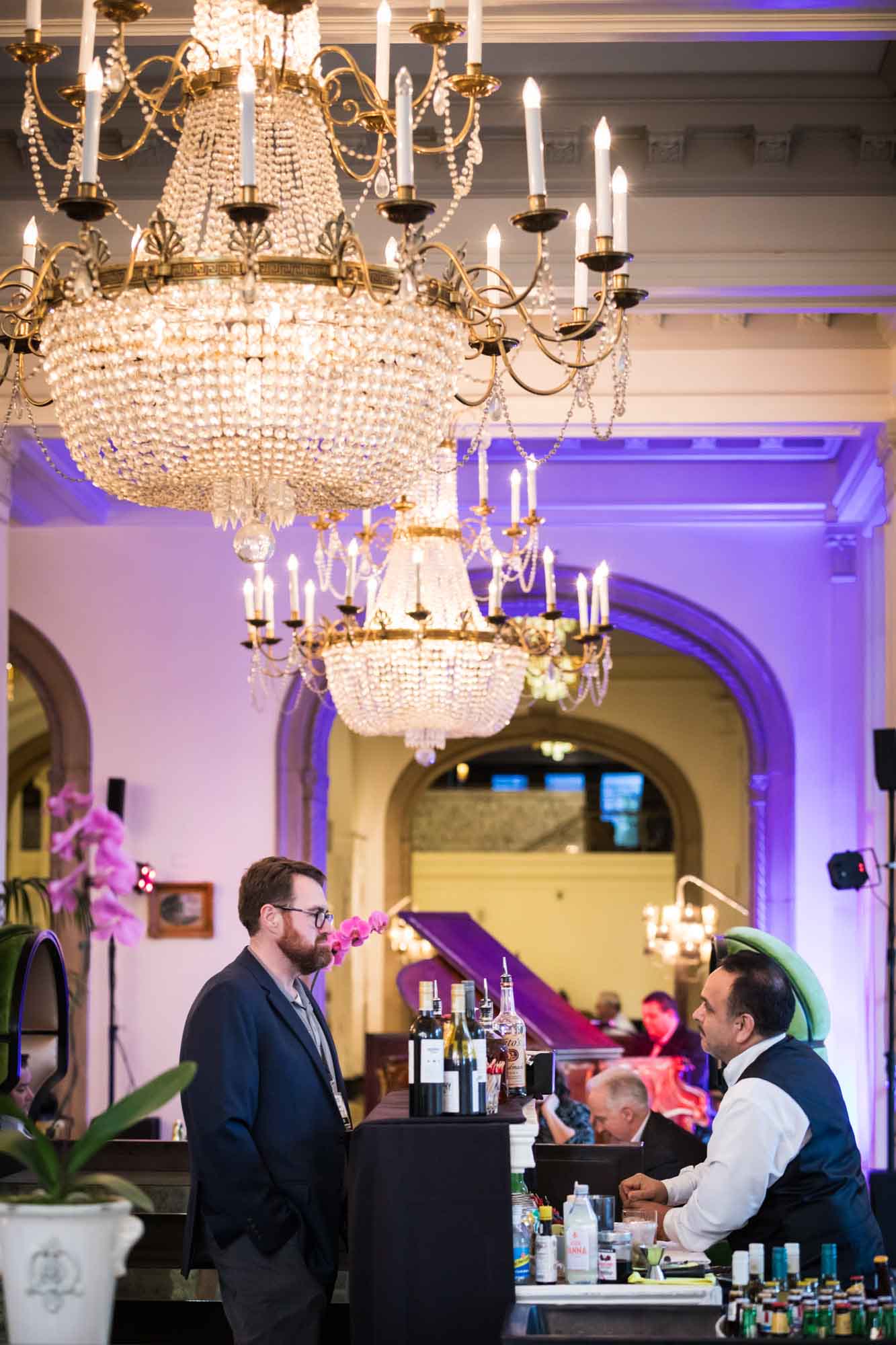 Man order a drink at a bar underneath a glass chandelier for an article on a St. Anthony Hotel corporate event