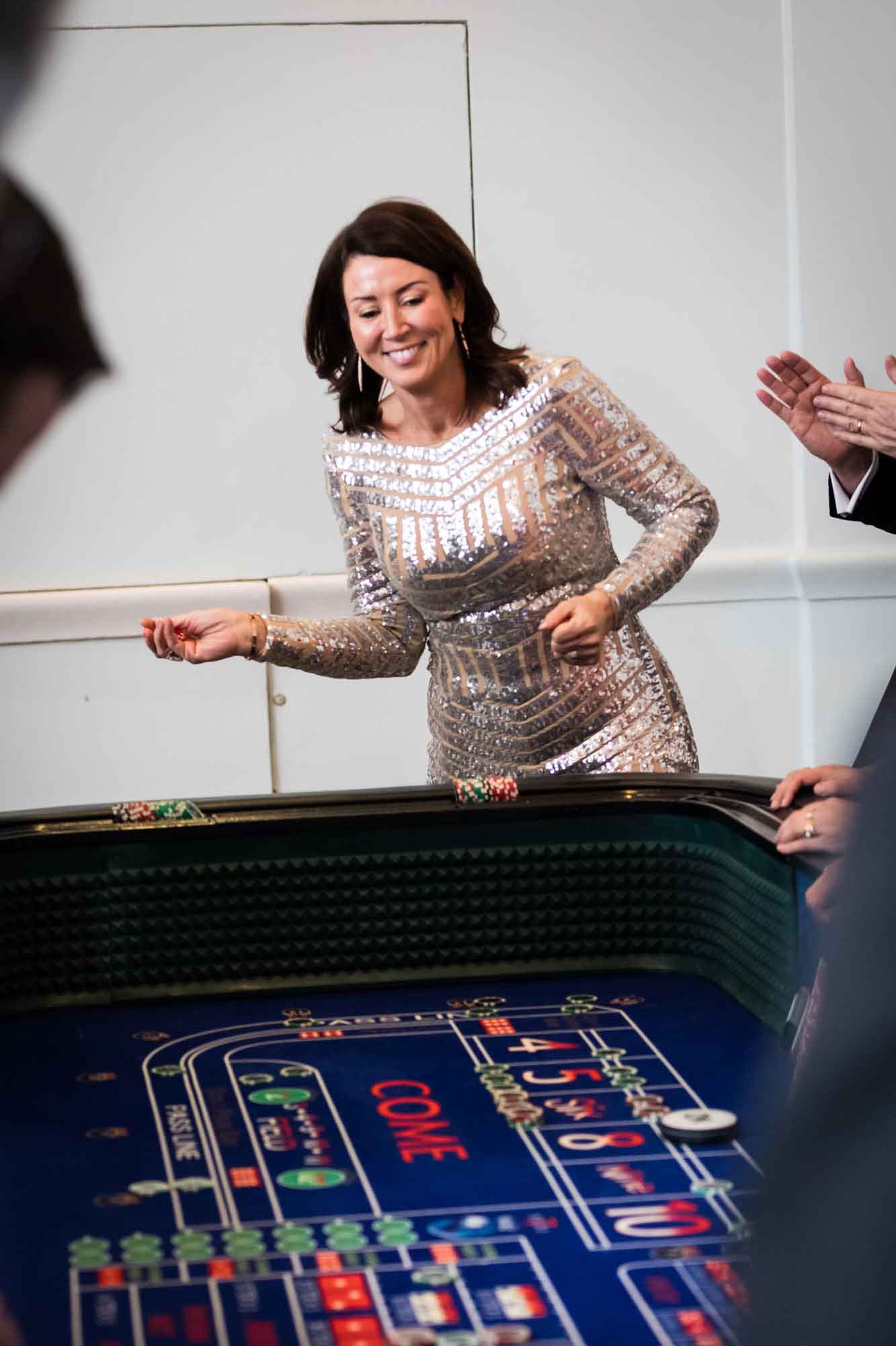 Woman wearing silver sequin dress about to throw dice at a crap table for an article on a St. Anthony Hotel corporate event