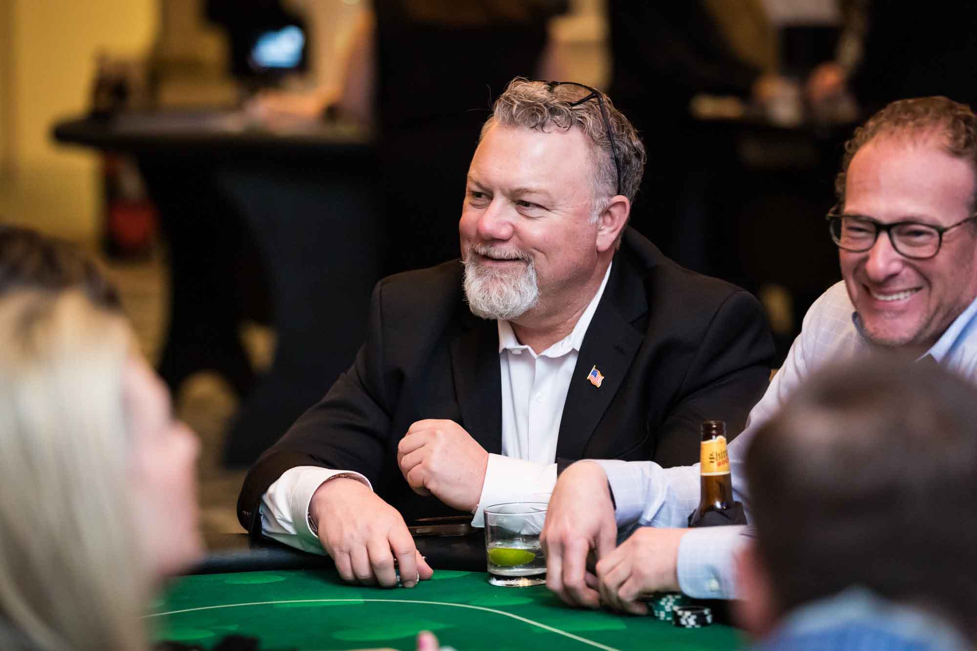 Two men sitting at a card table holding poker chips sitting with drinks in front of them for an article on a St. Anthony Hotel corporate event