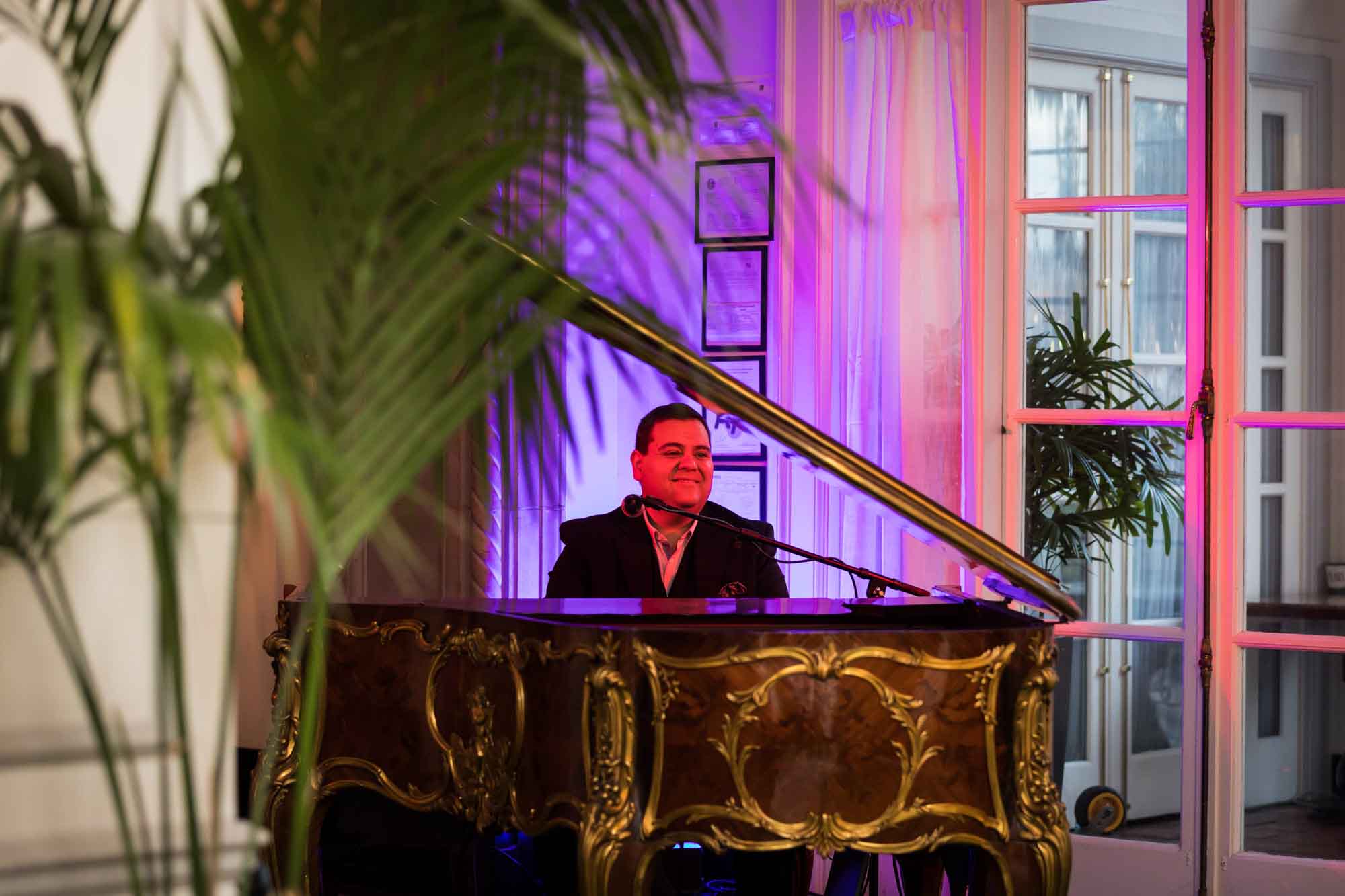 Piano player bathed in red light playing at vintage piano for an article on a St. Anthony Hotel corporate event