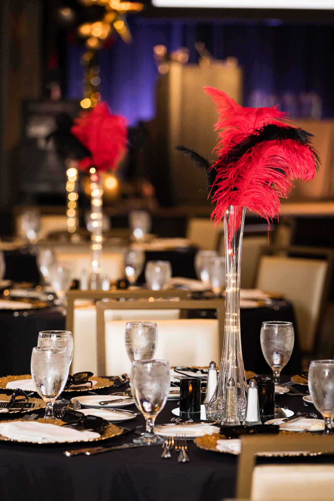 Close up of tables set for dinner with red and black feather centerpieces for an article on a St. Anthony Hotel corporate event