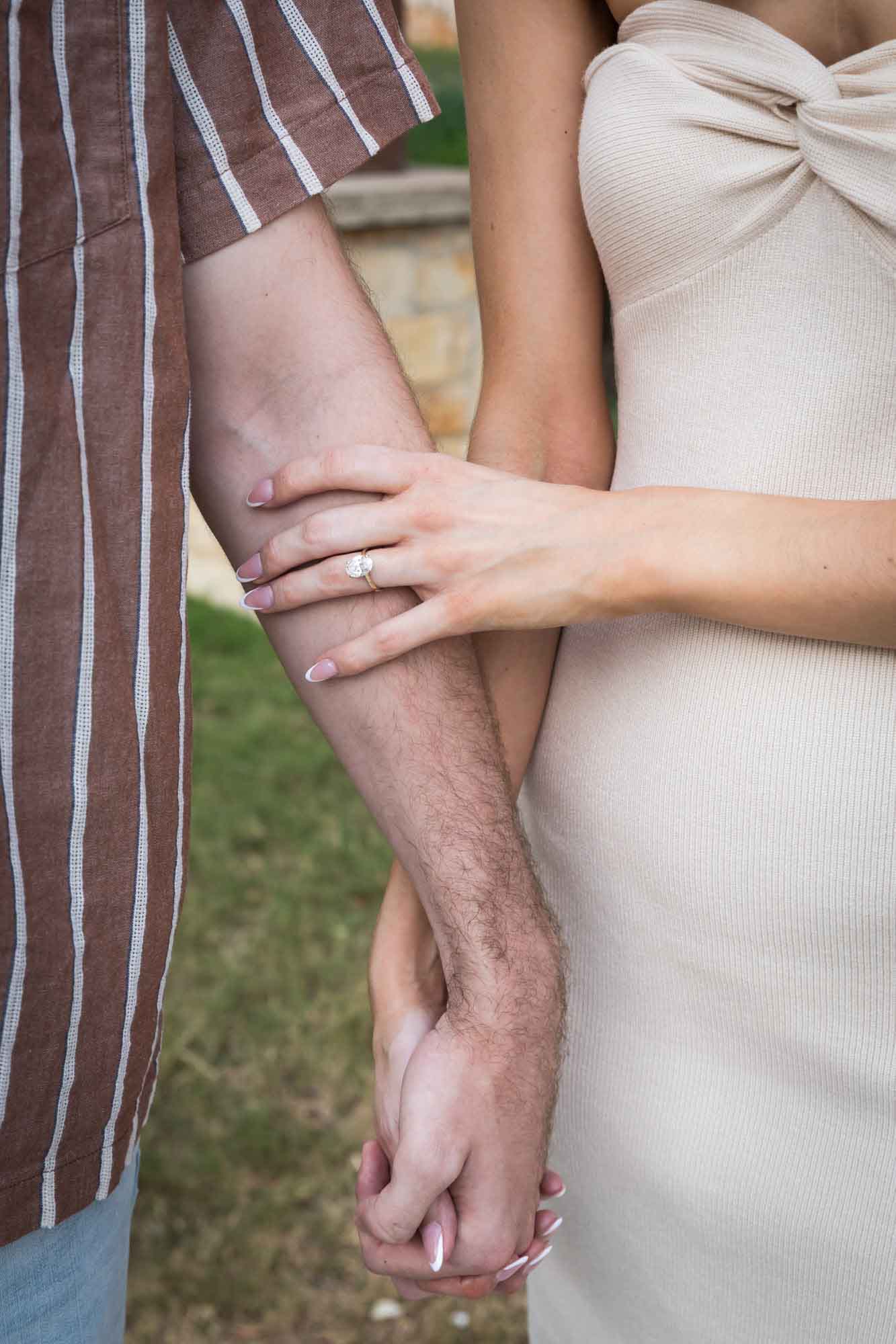 Close up of couple holding hands showing woman wearing engagement ring