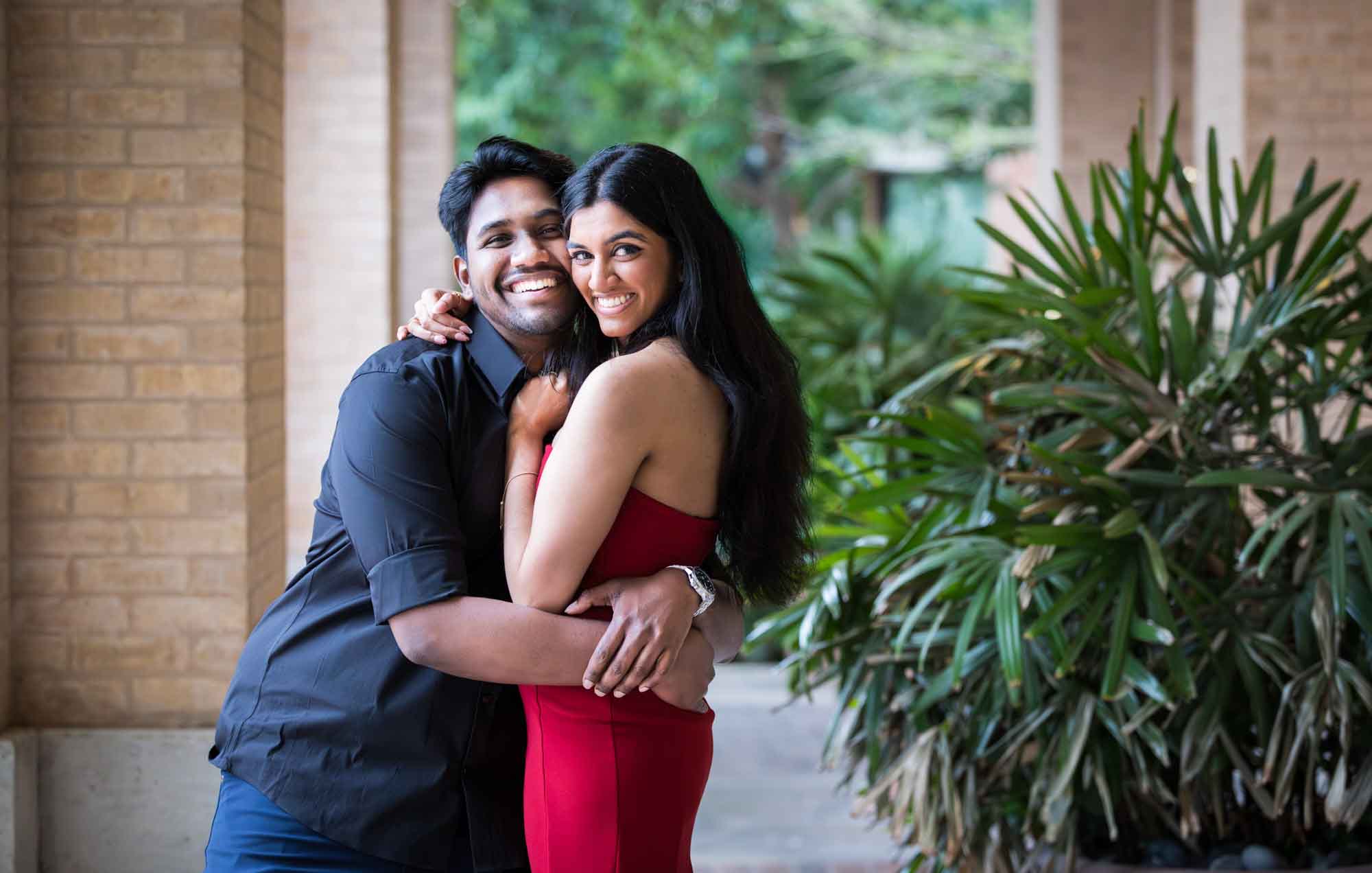 Couple hugging under vaulted archway beside a green palm plant during a Pearl surprise proposal
