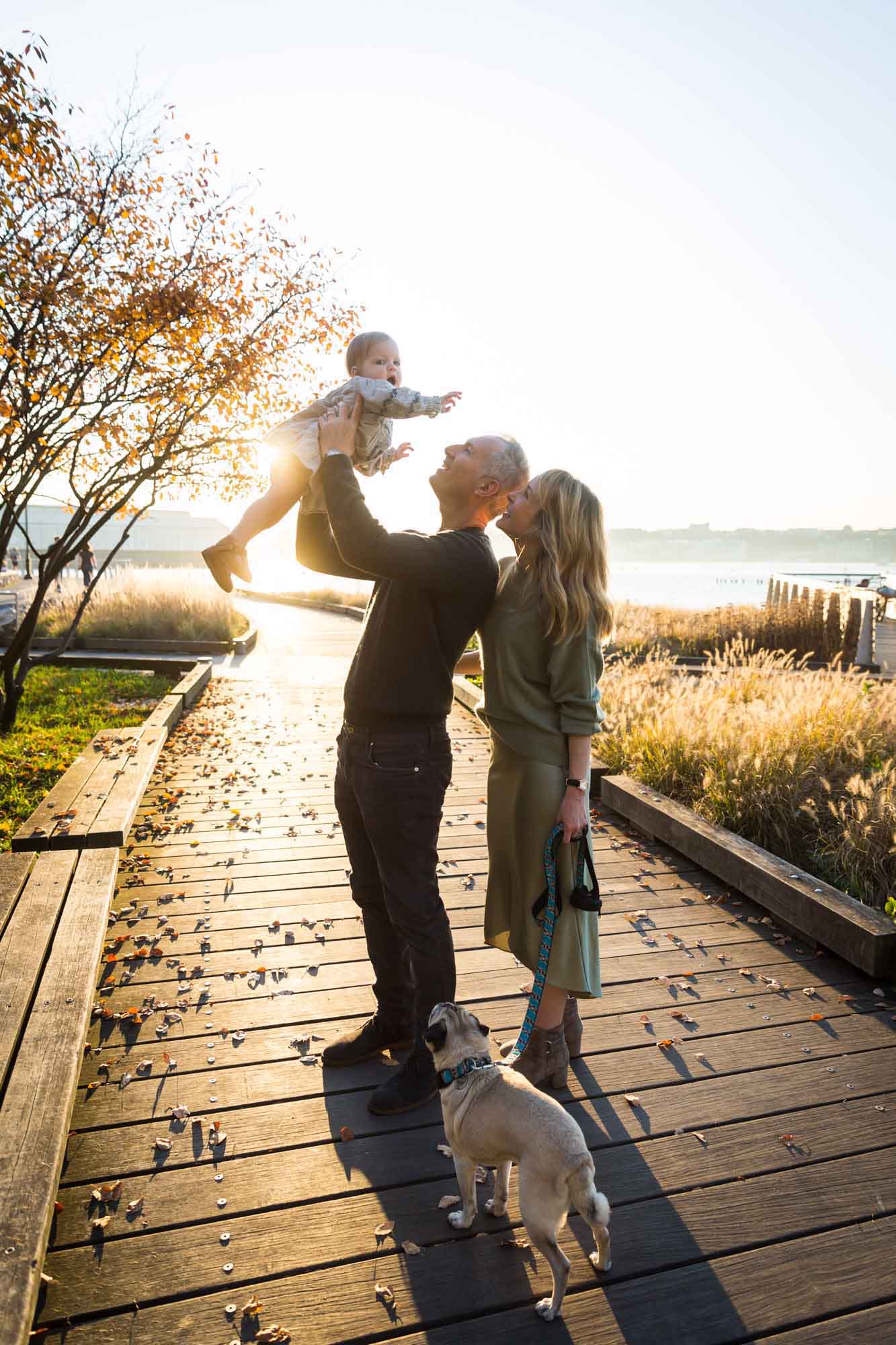 Backlit photo of parents holding little girl in the air in Riverside Park