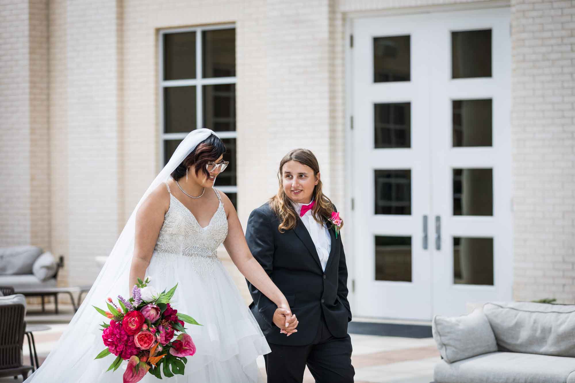 Cornerstone Church wedding photos of bride wearing sleeveless dress and holding flower bouquet holding hands with groom while walking in courtyard