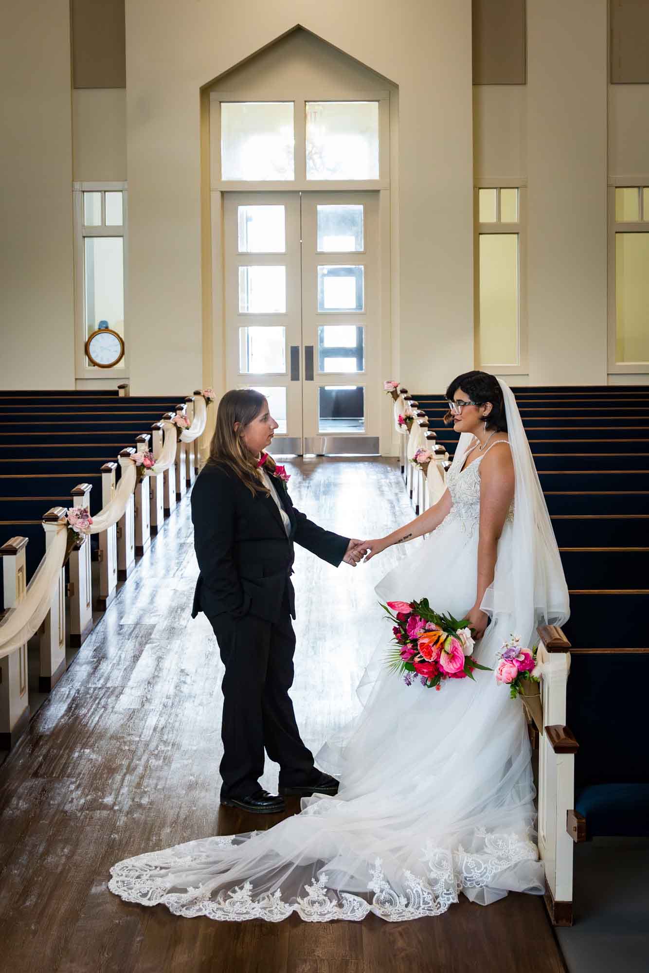 Bride and groom holding hands while leaning against pew in Vada Hagee Prayer Chapel