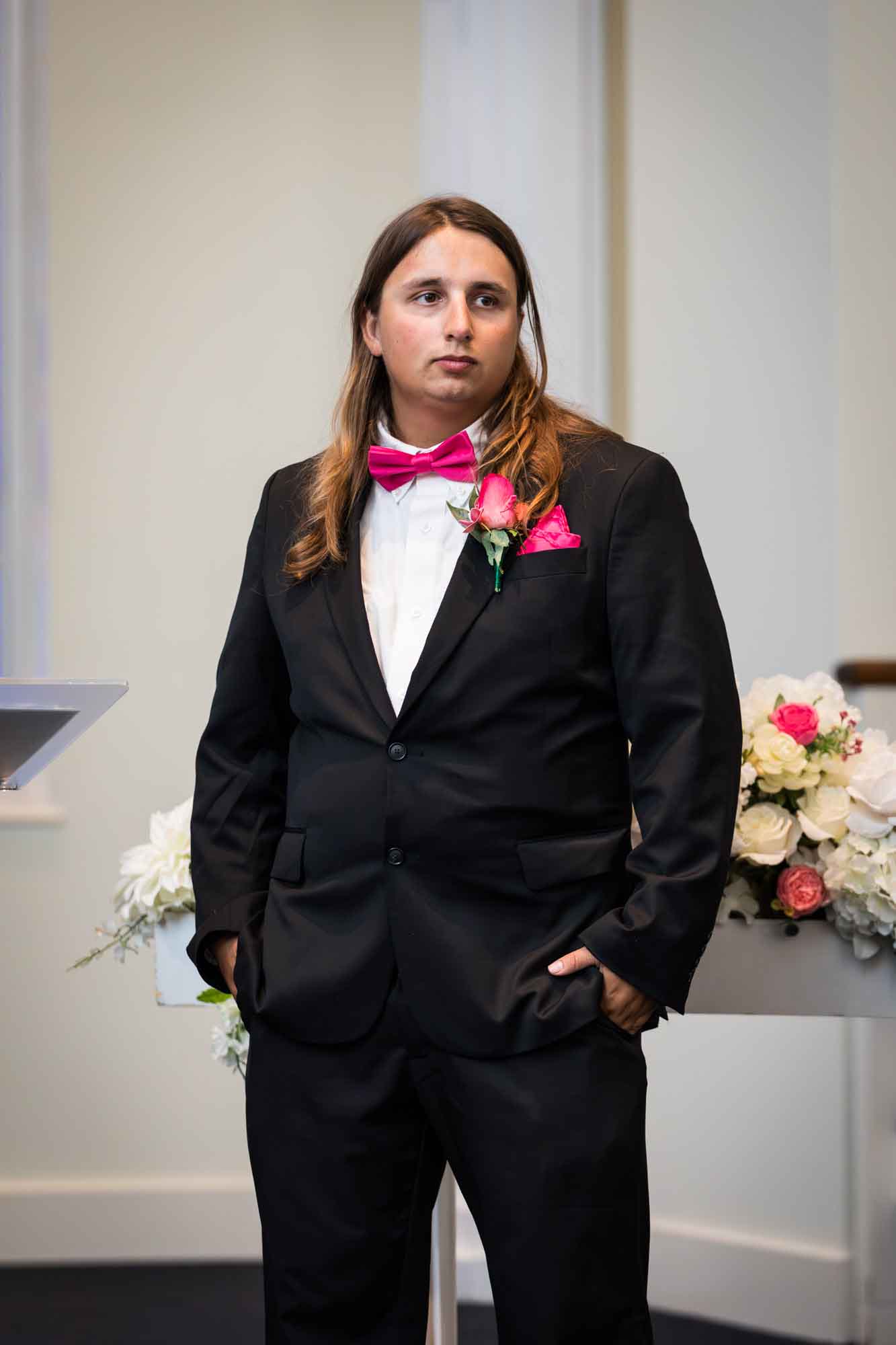 Cornerstone Church wedding photos of groom wearing black suit and pink bow tie with white flowers in background