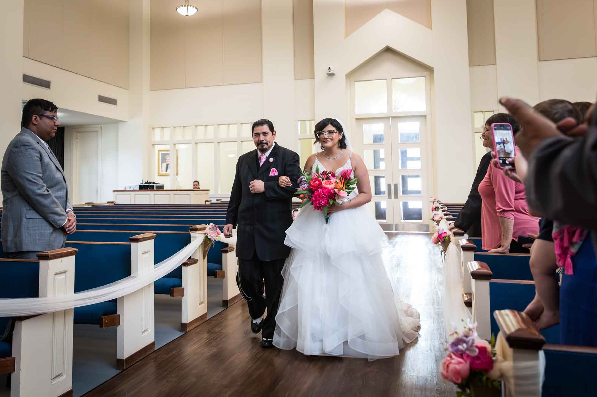 Cornerstone Church wedding photos of bride holding flower bouquet and father walking down aisle in front of guests during ceremony