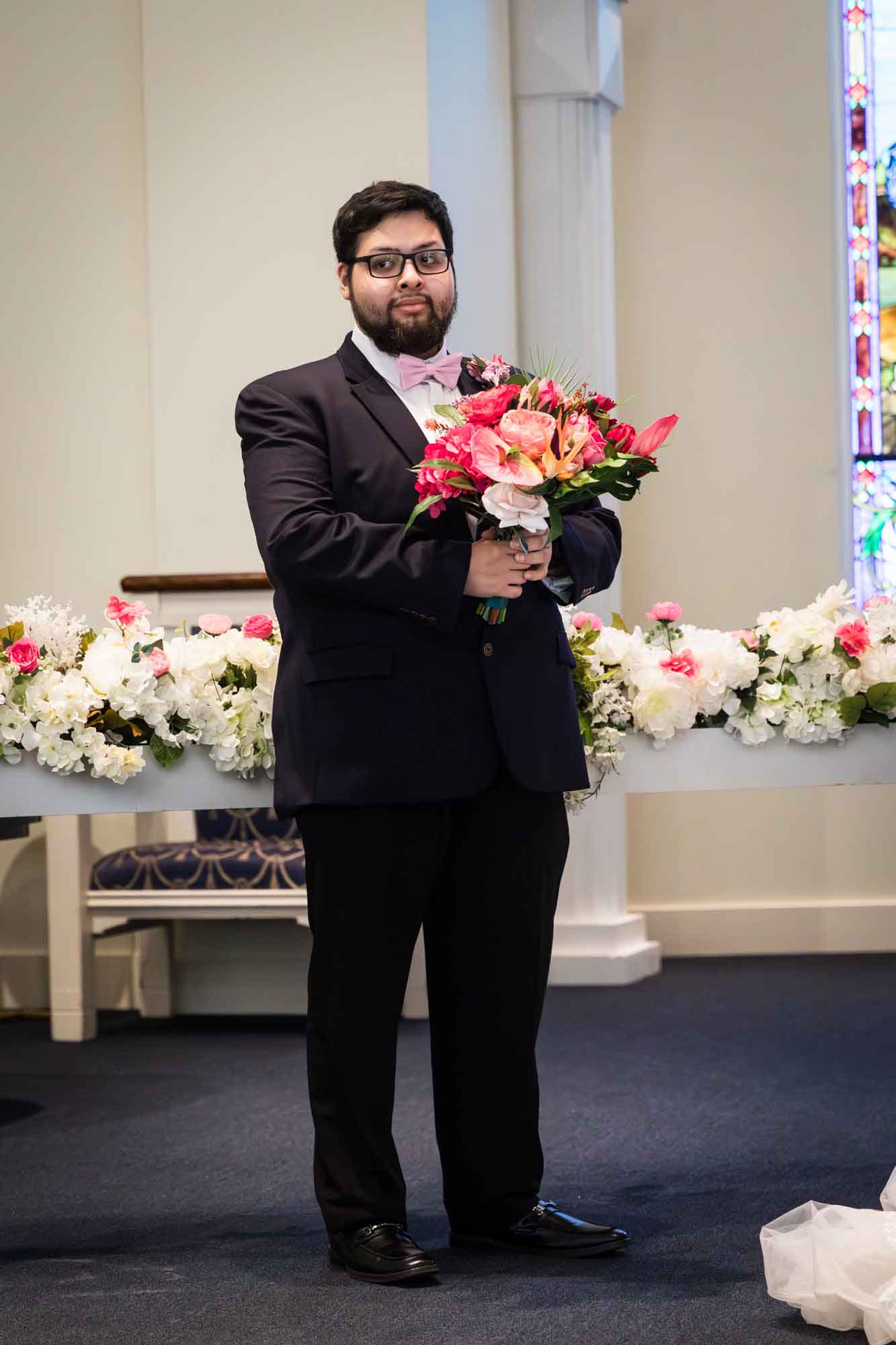 Cornerstone Church wedding photos of groomsman wearing black suit and pink bow tie holding flower bouquet