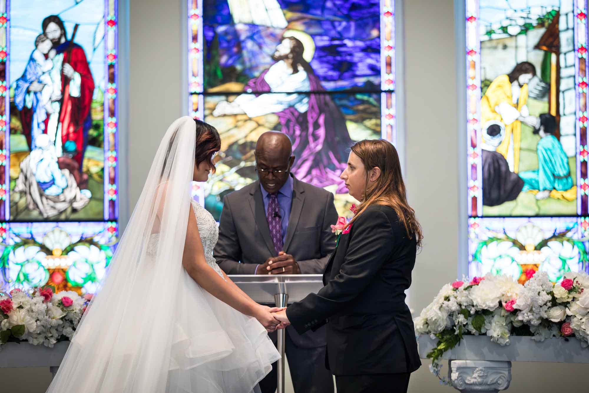 Cornerstone Church wedding photos of bride and groom holding hands in front of African American officiant standing at podium with stained glass windows in background